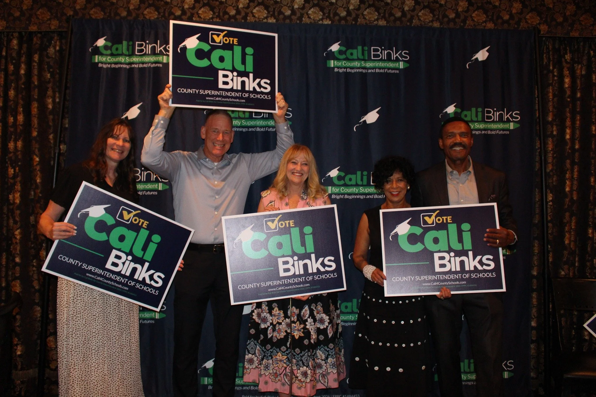 Cali Binks with four guests holding a yard sign promoting her campaign.