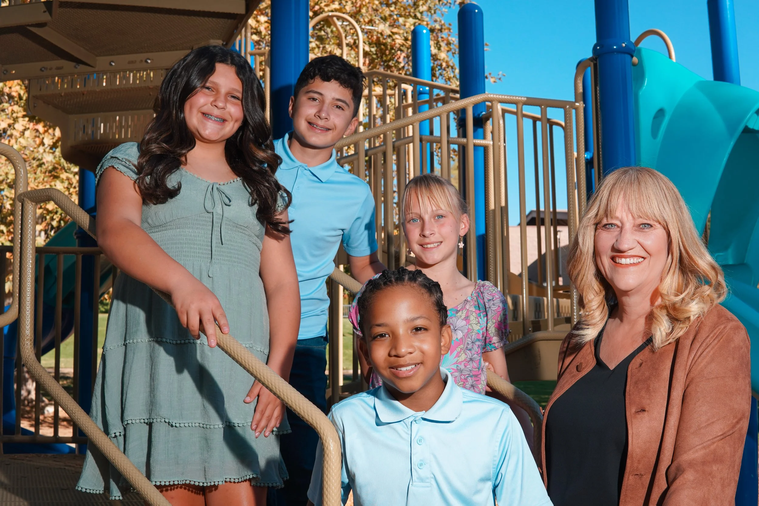 Cali posing next to three young students next to a playground structure.