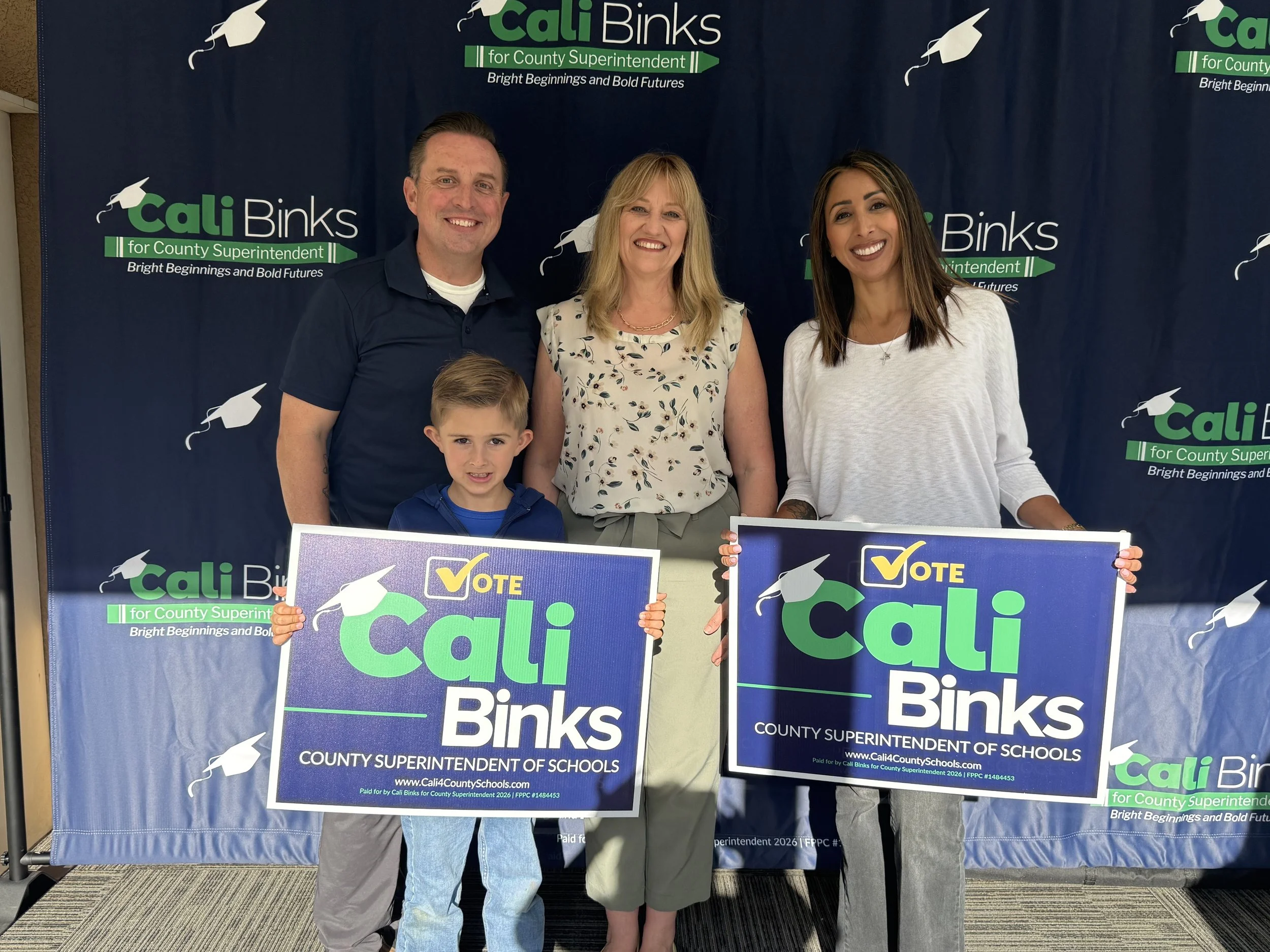 A family of three holding yard signs with Cali