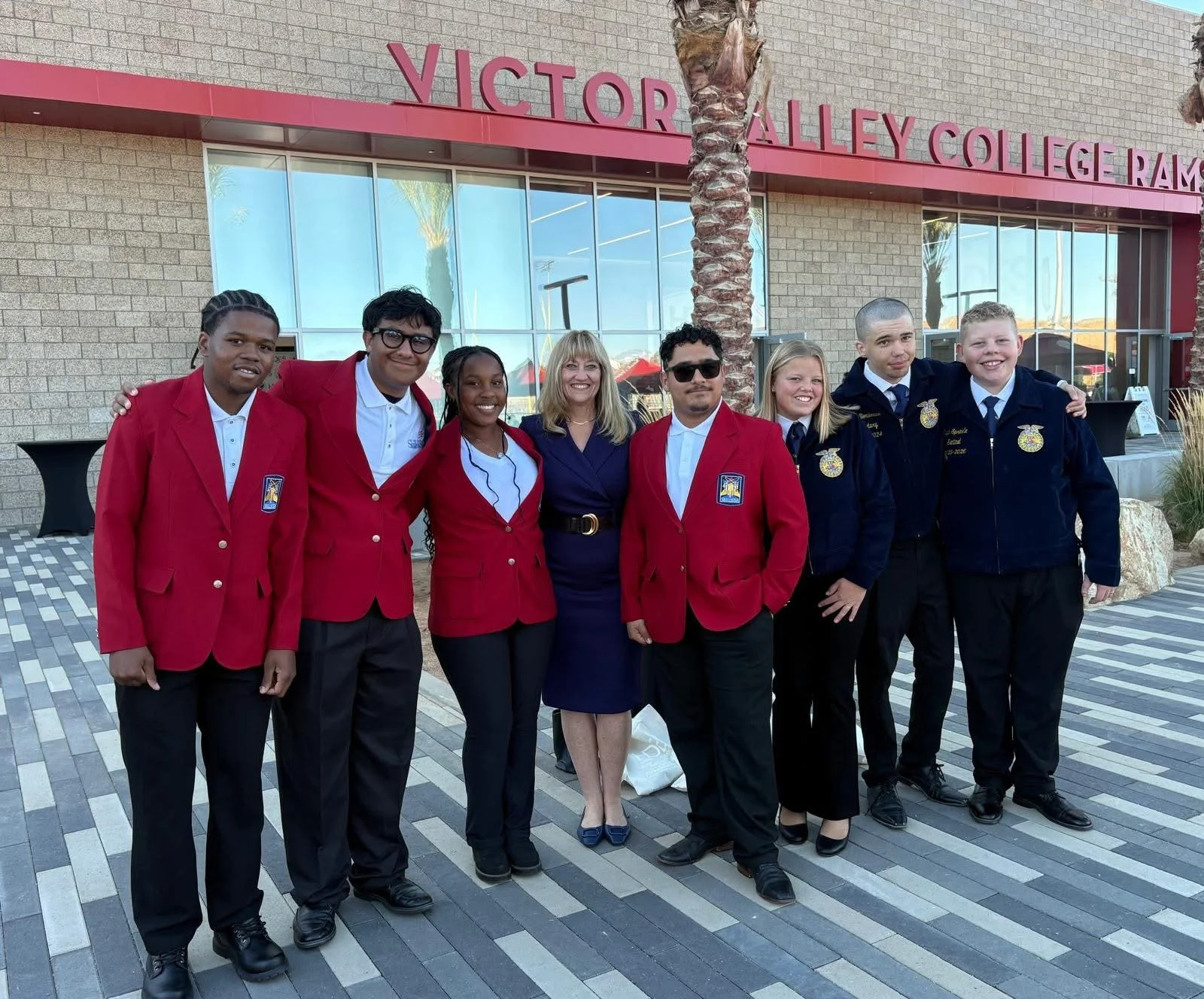 Seven high school students surrounding Cali and smiling in front of Victor Valley College.