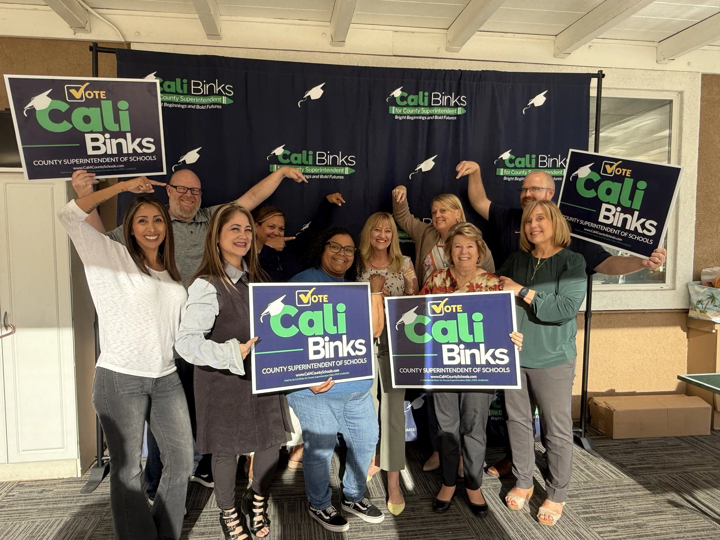A group of community members holding yard signs and pointing at Cali