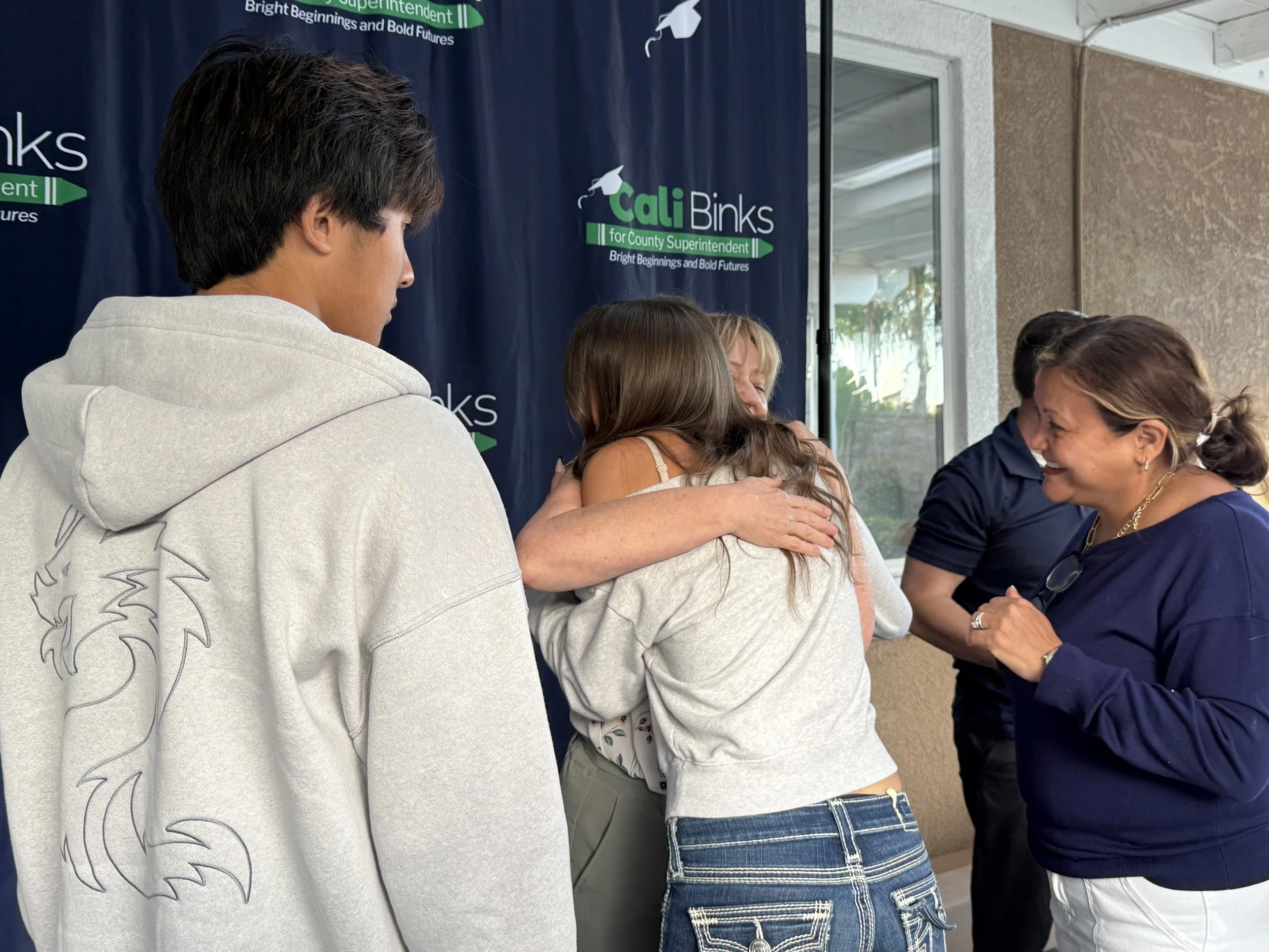Cali hugging a high school student while another high school student and an adult watch
