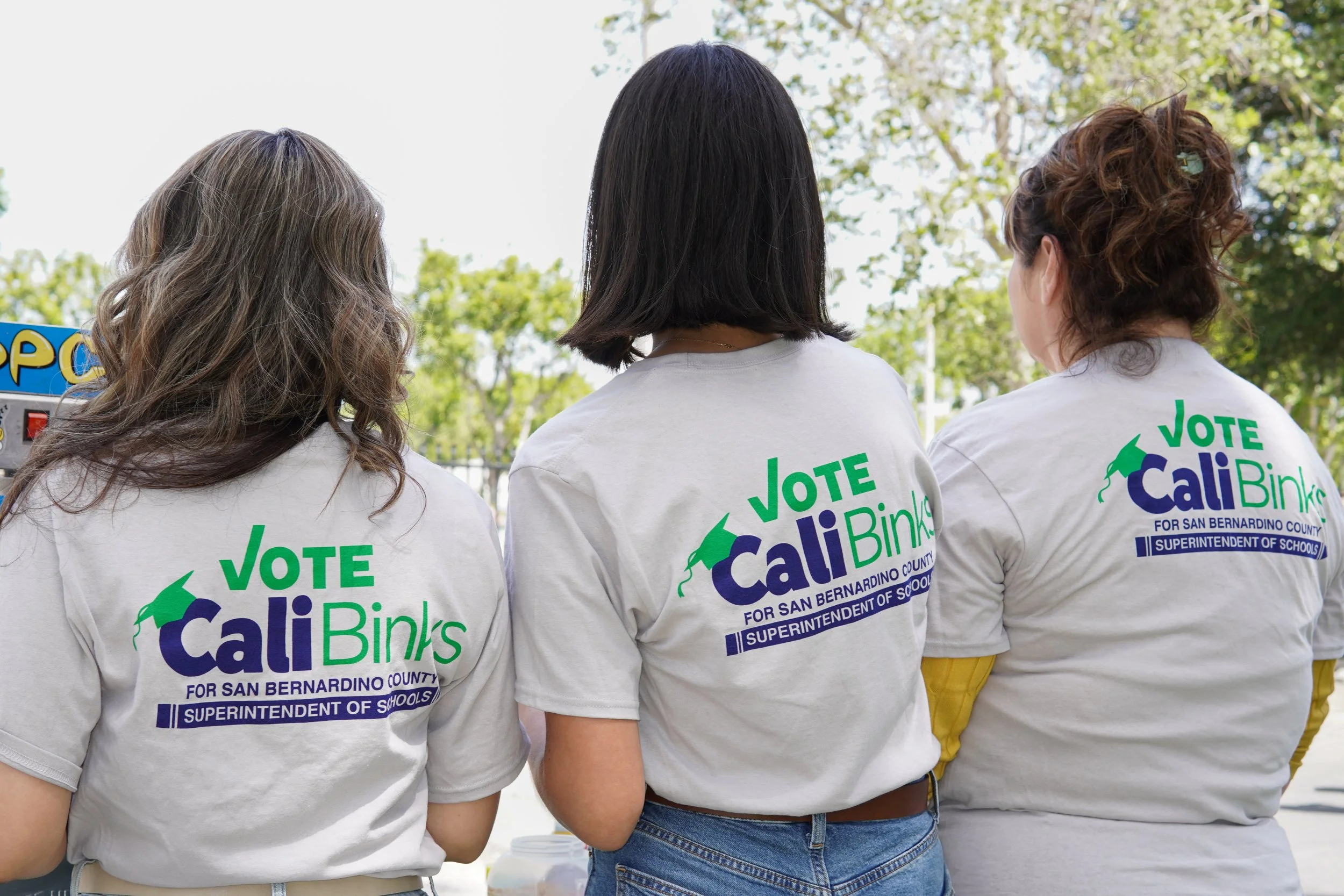 Three adults showing the Cali Binks campaign t-shirt facing away from the camera in a row.