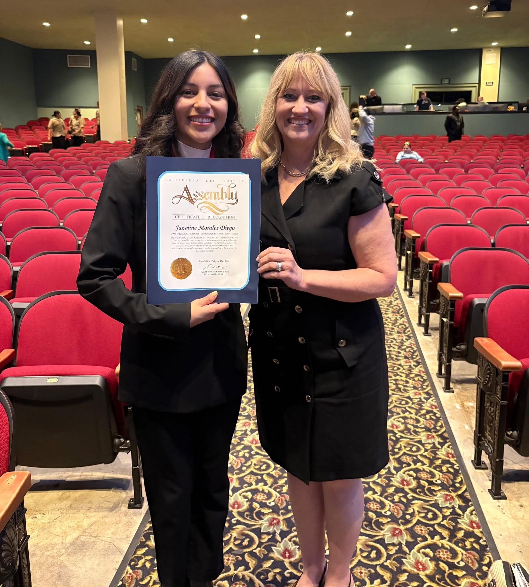 Teenage student holding a certificate next to Cali while smiling.