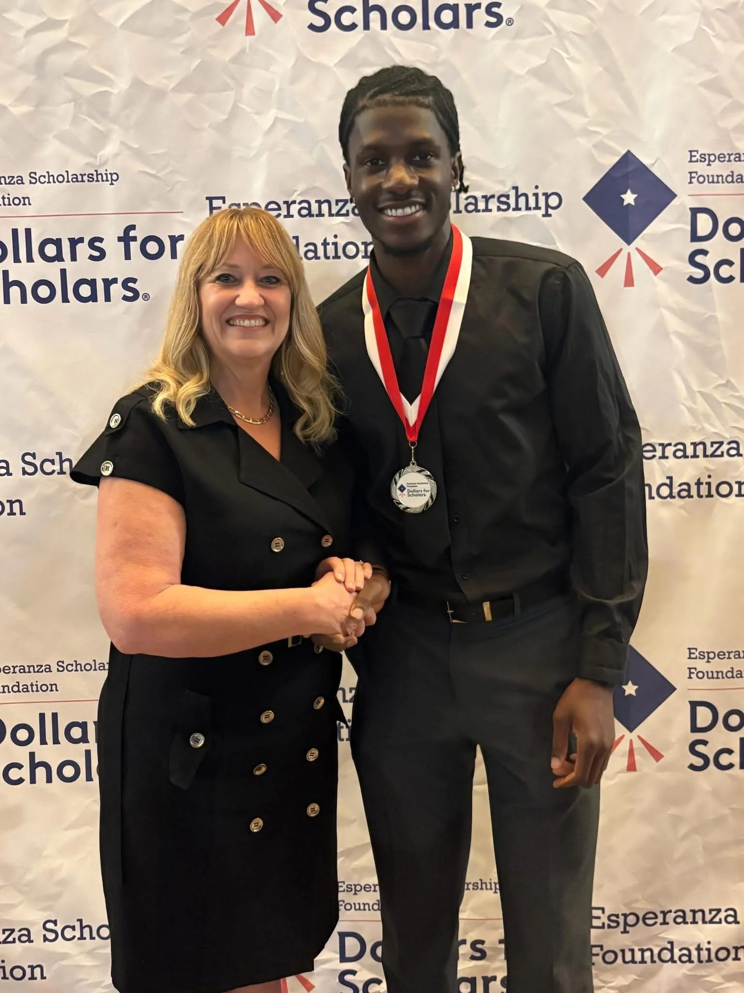 Cali standing next to a teenage student wearing a medal around their neck while they smile.