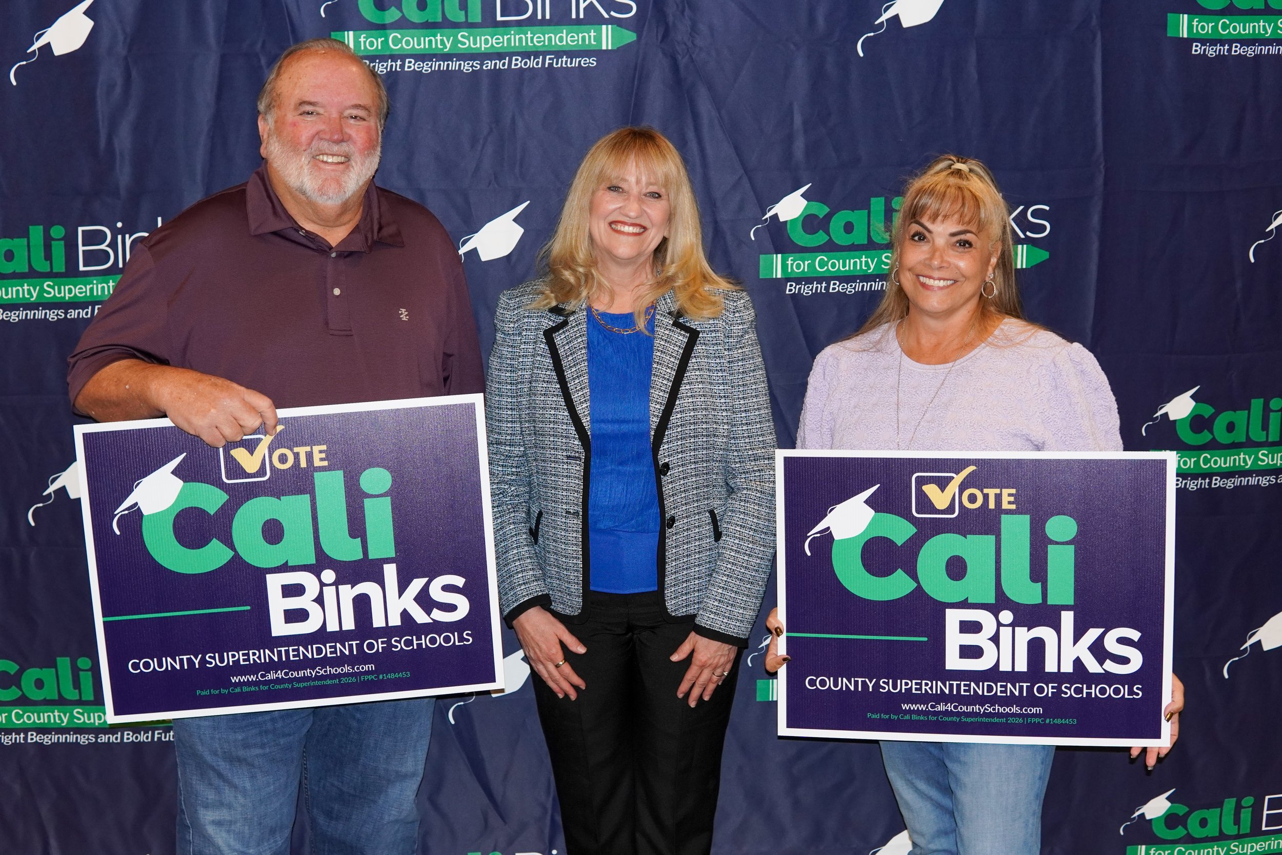 Cali posing for a photo with two adults holding yard signs. 
