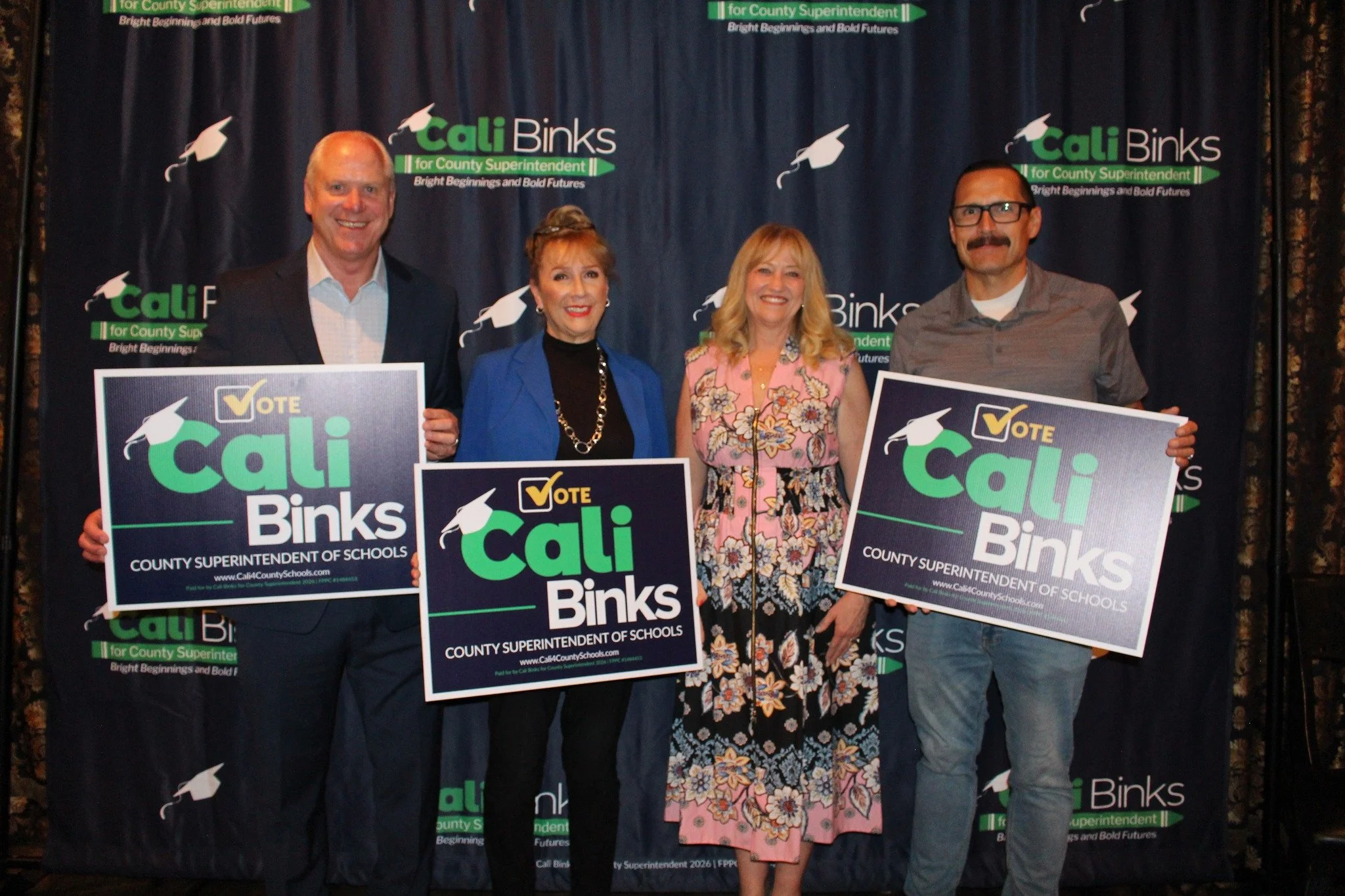 Cali Binks with two guests and husband holding a yard sign promoting her campaign.