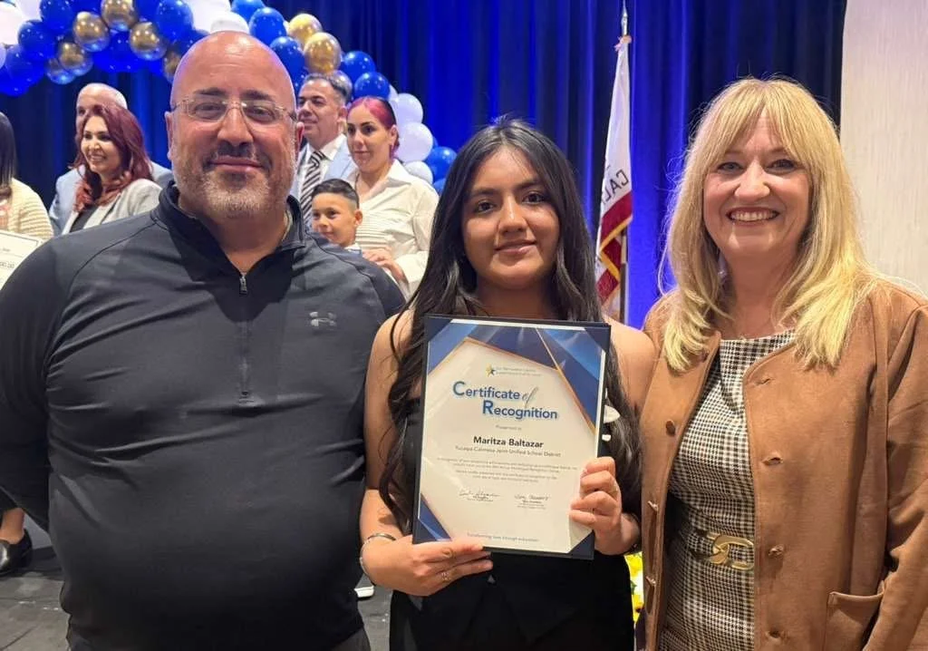 A high school student and their father smiling and holding a certificate next to Cali.