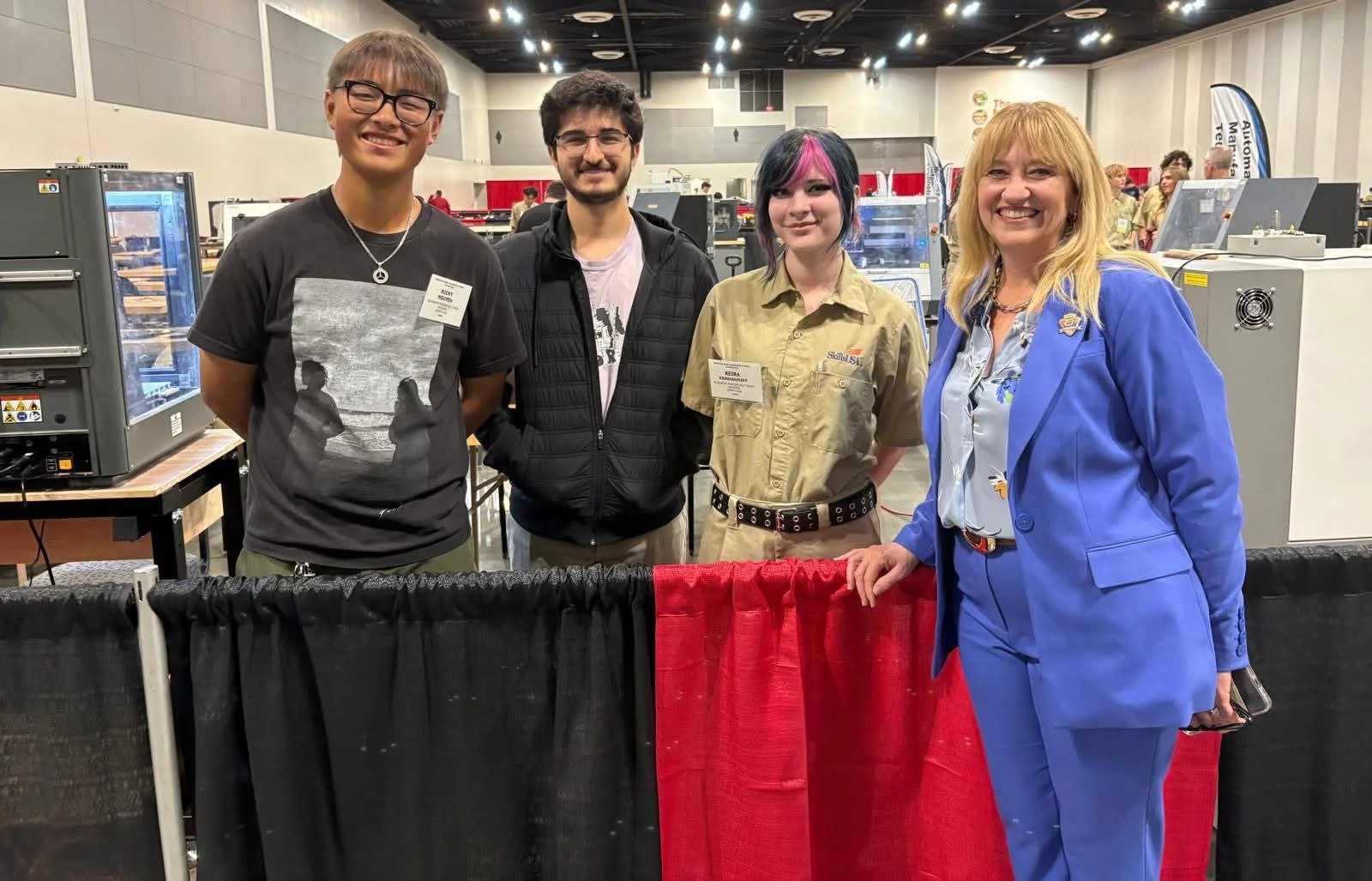 Three high school students at Skills USA next to their project standing and smiling next to Cali.