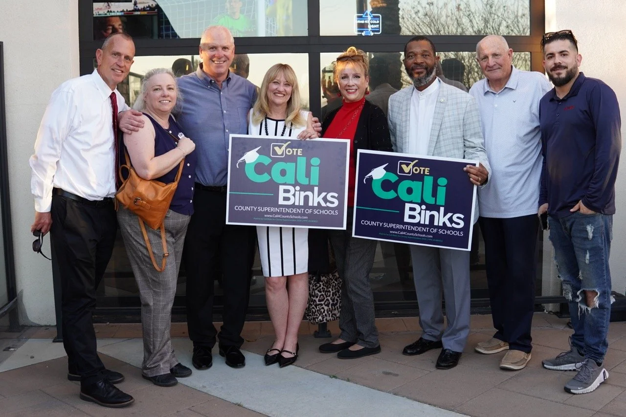 Cali Binks posing for a photo with six guests and her husband while holding yard signs.