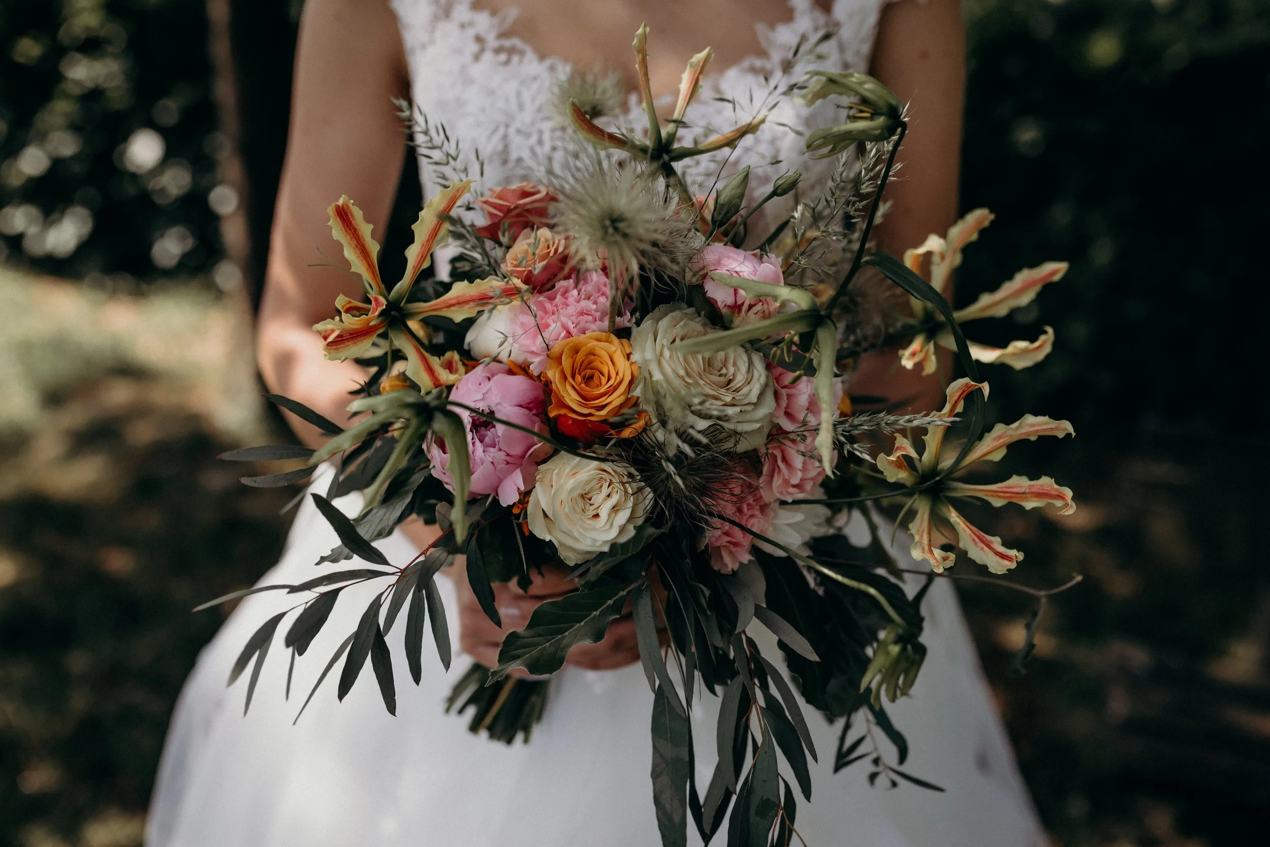 A woman in a white dress holding a large bouquet of mixed flowers including roses and greenery.