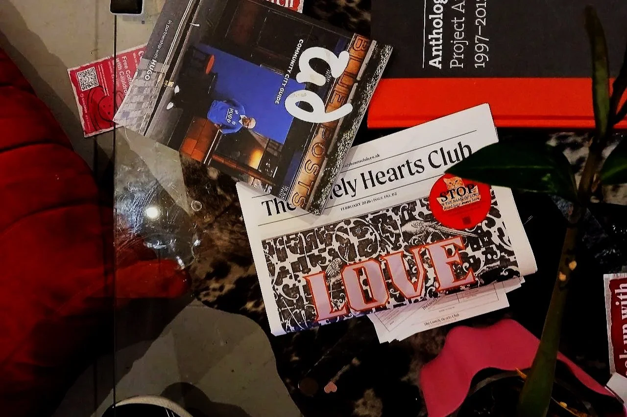 Glass table with multiple print magazines and a folded copy of The Lonely Hearts Club Newspaper Issue 02 LHC.