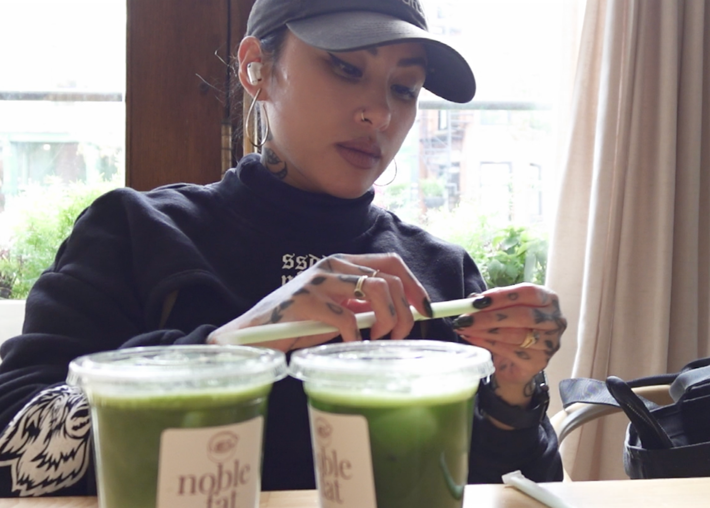 Jules in a cafe opening a straw to enjoy two matcha drinks