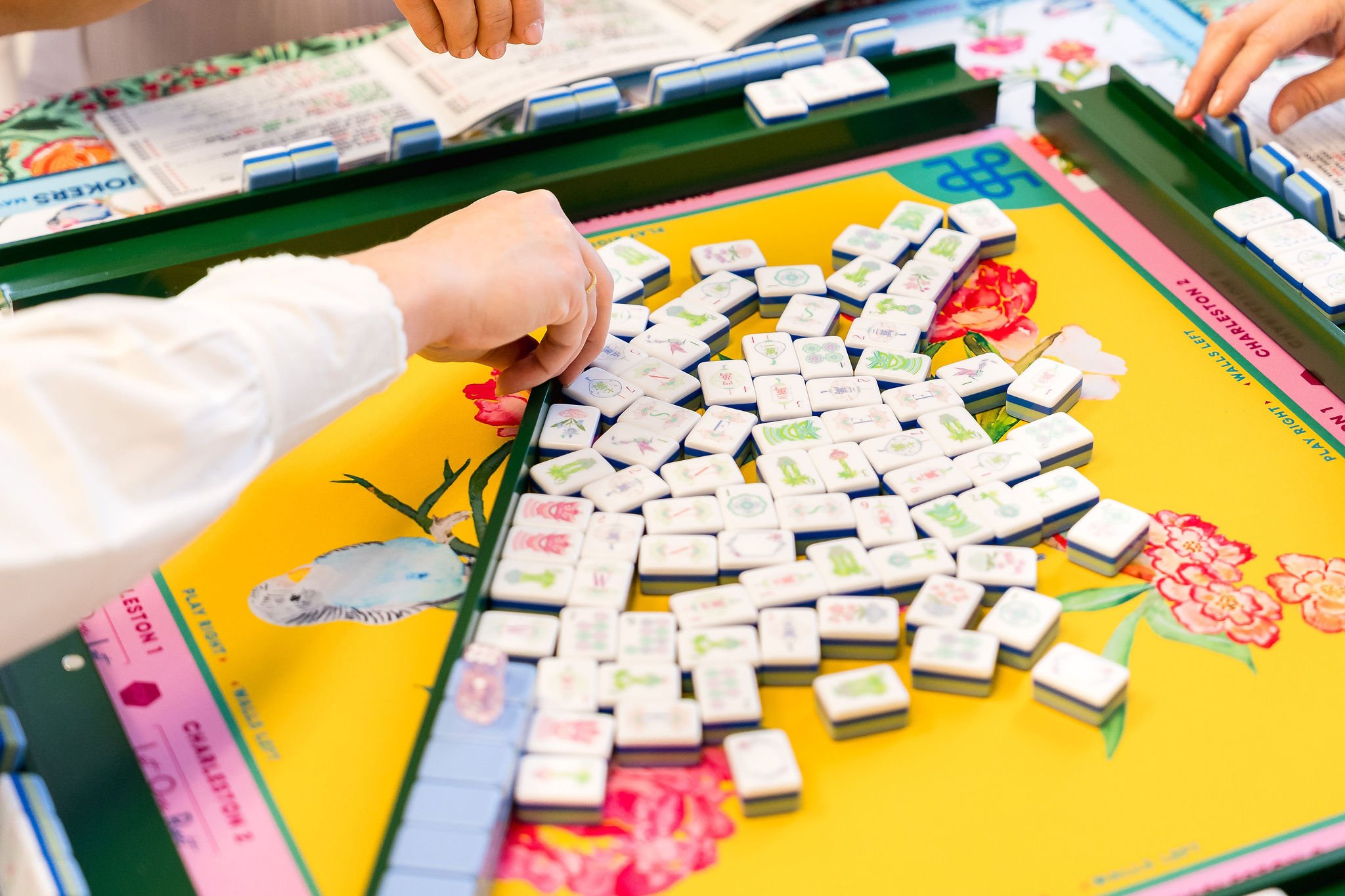 People playing a game of Mahjong, with tiles on a colorful yellow and pink game board.