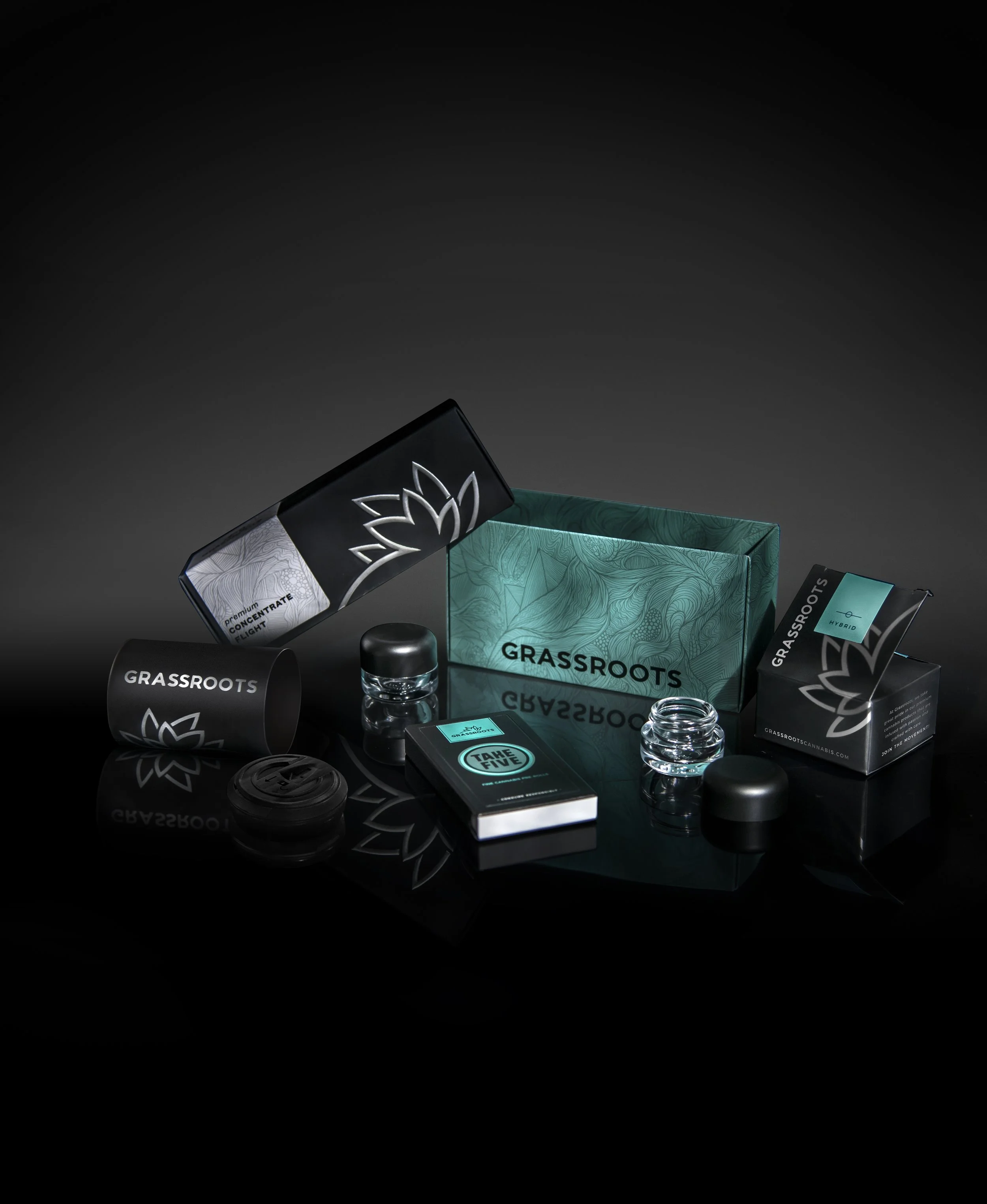 Cannabis product packaging and accessories, including jars, a pack of rolling papers, and a black box, on a black reflective surface