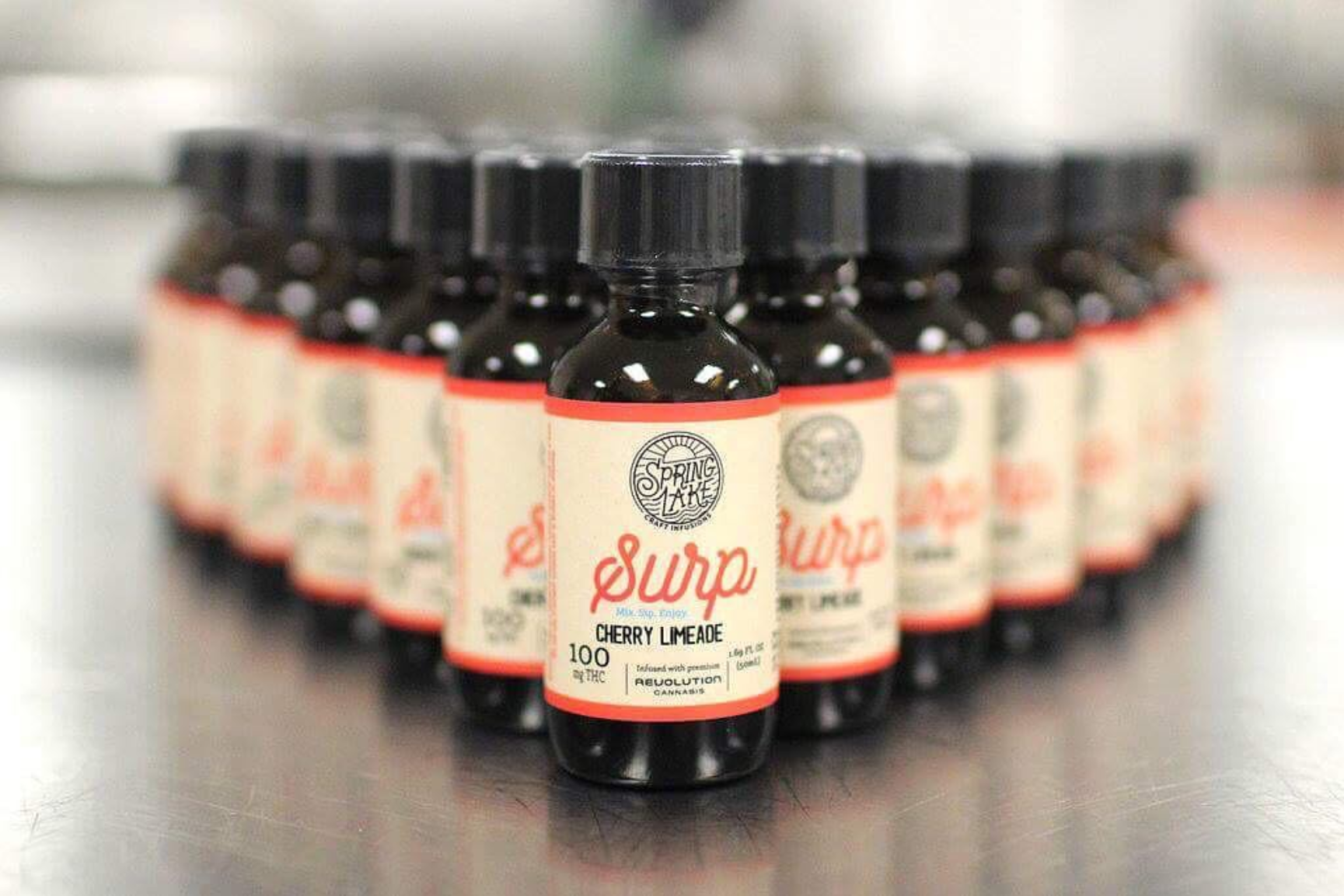 Multiple small bottles of Spring Lake Surp Cherry Limeade flavor arranged in a cluster on a metallic surface.