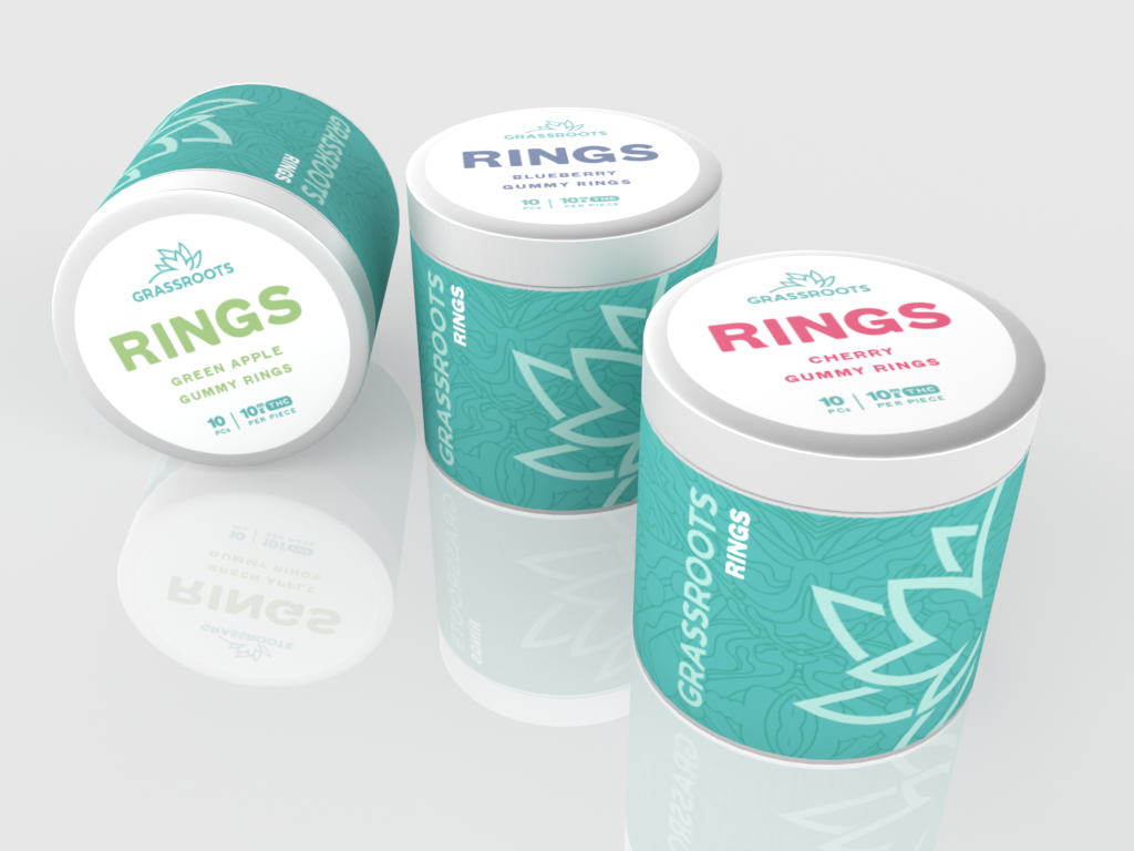 Three cylindrical containers of Grassroots gummy rings, including Green Apple and Cherry flavors, with blue backgrounds, white lids, and colorful text.