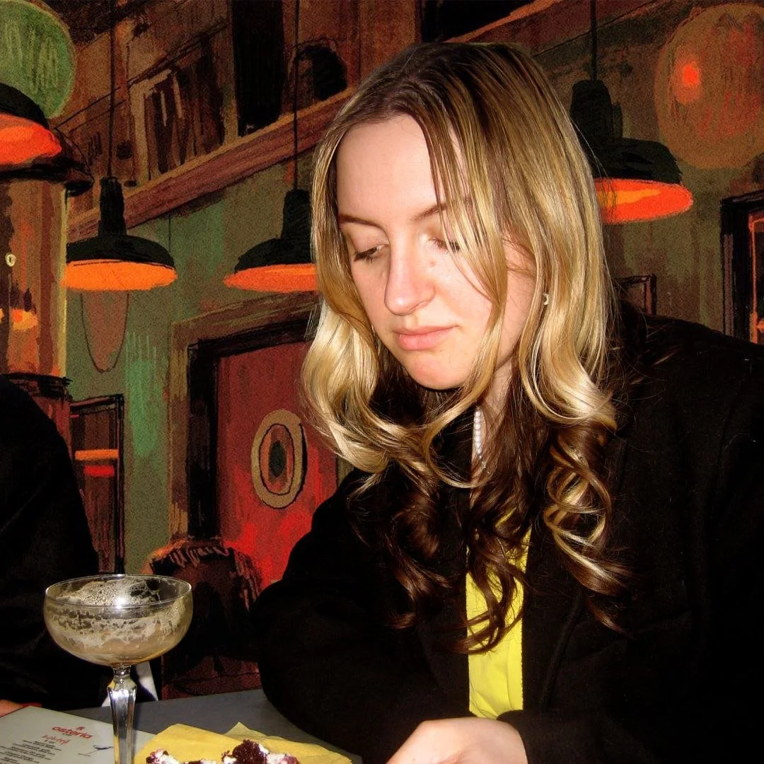 A young woman with long curly blonde hair looking down at a dessert in front of her at a restaurant.