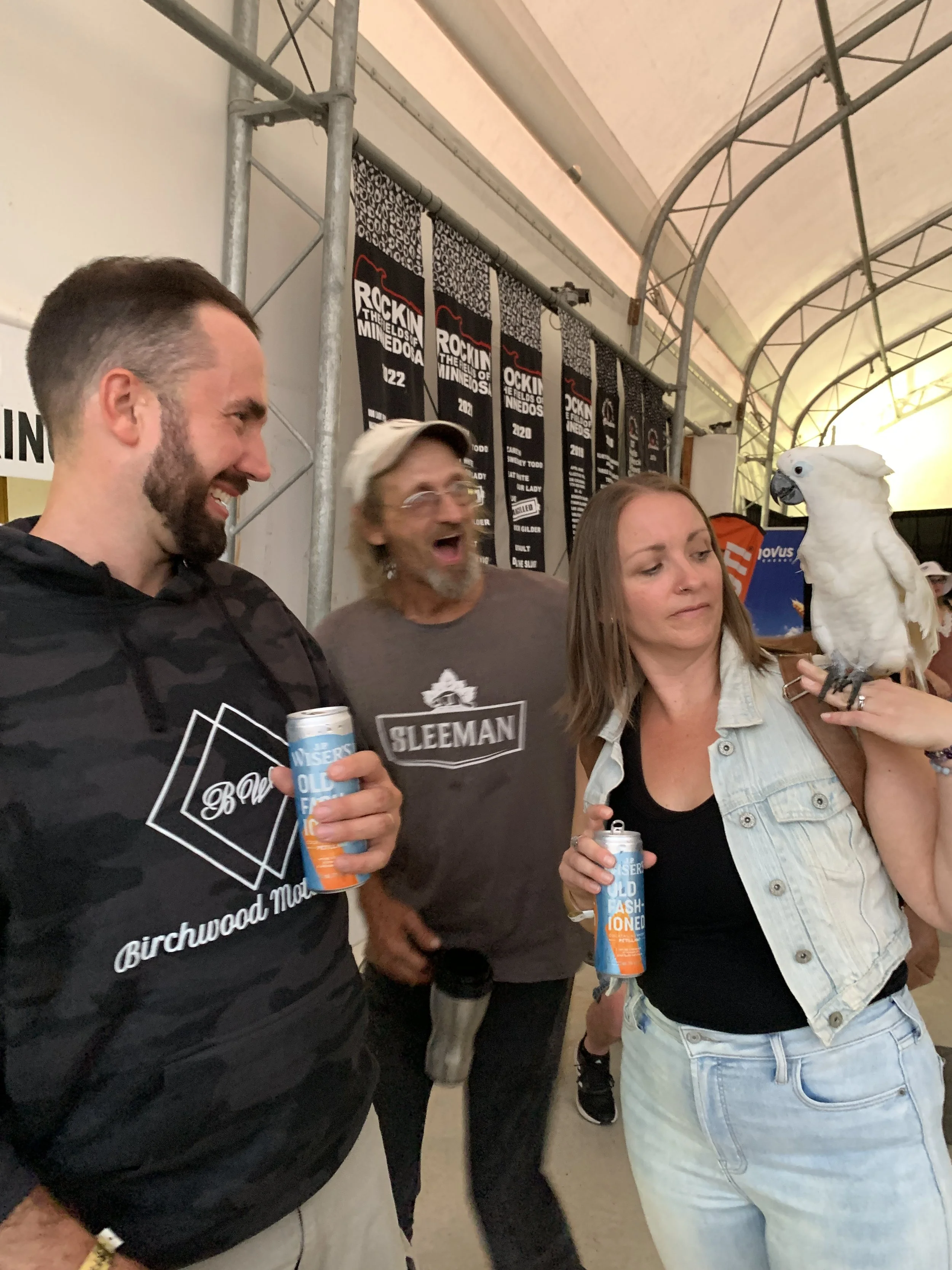 People at a festival holding drinks and looking at a white cockatoo bird perched on Megan Deaust's arm.