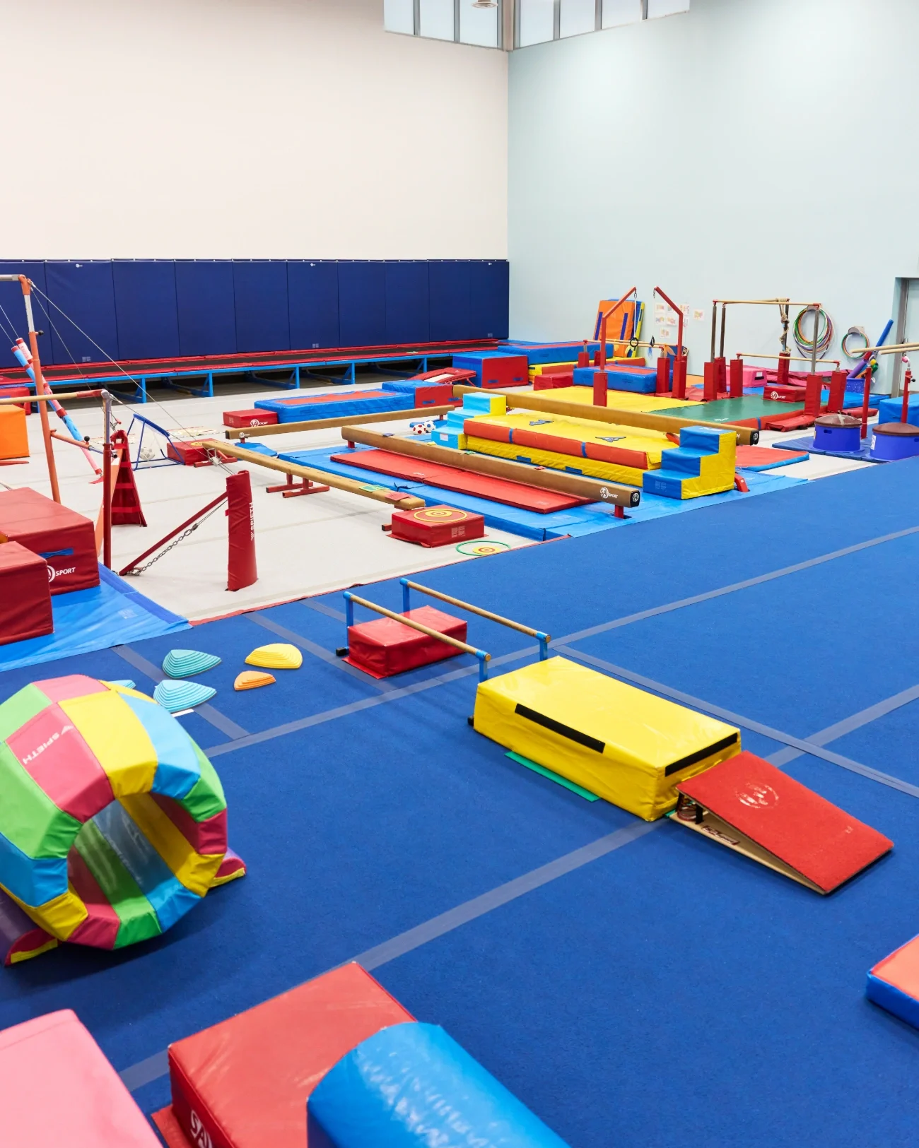 Interior of Milton Springers with various padded mats, balance beams, bars, and foam obstacles in bright colors.