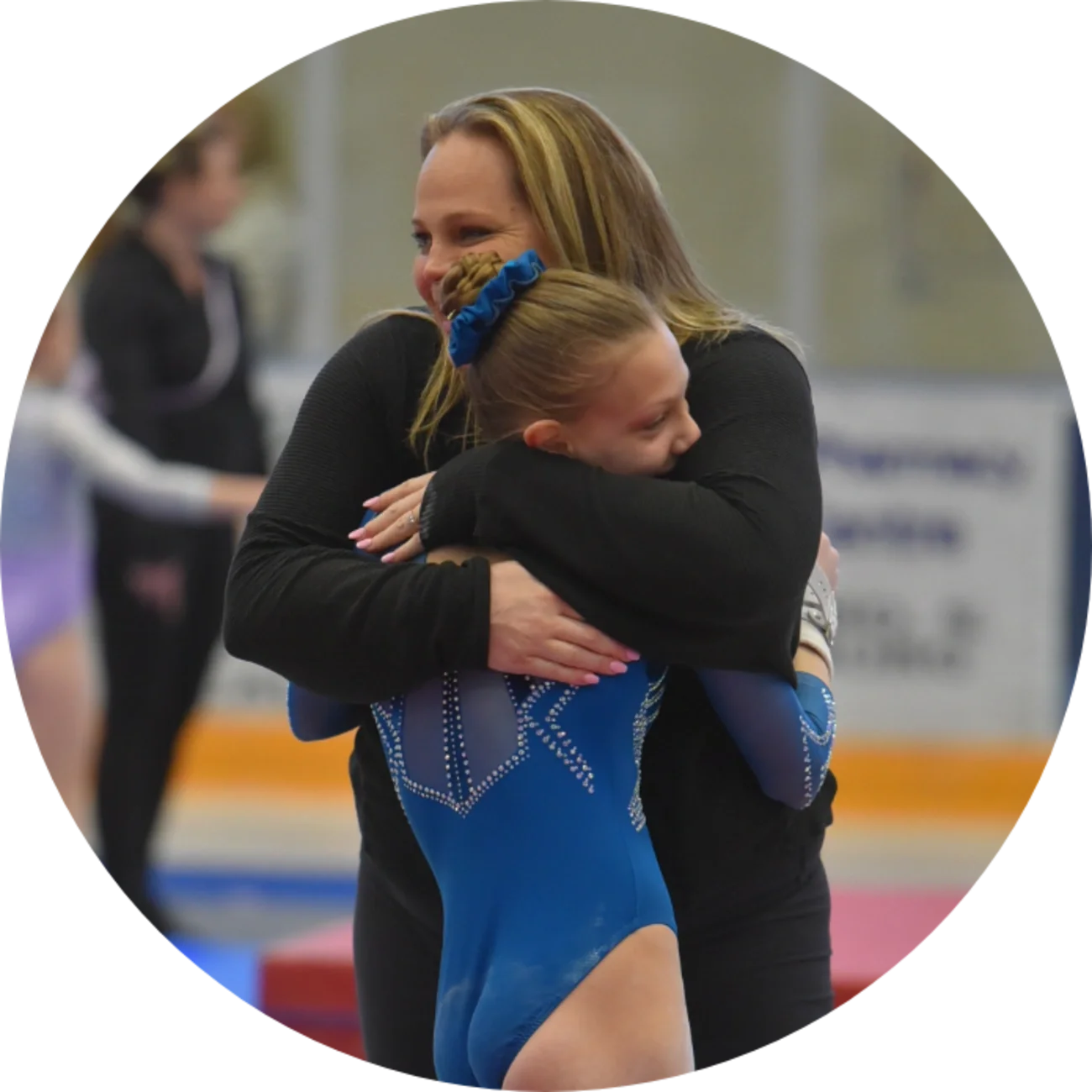 A young female gymnast hugging a woman in a gymnasium.