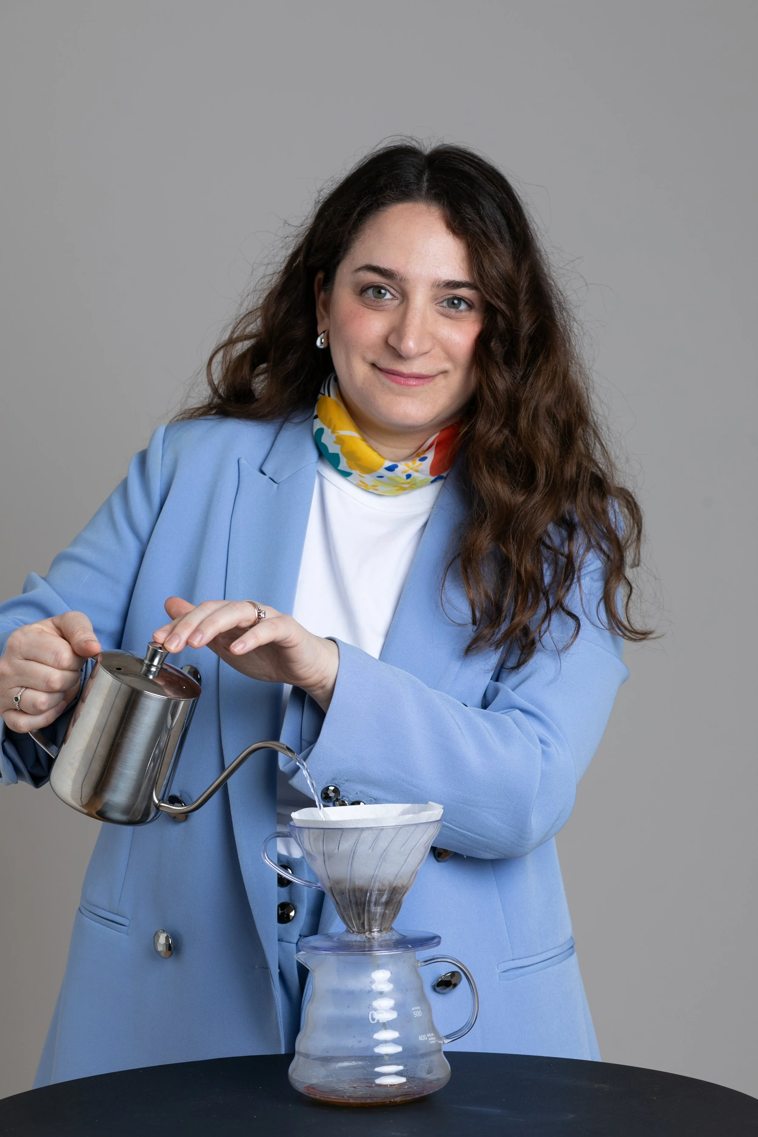 Mujer con cabello rizado y vestimenta azul realizando una prueba de filtración de café en un laboratorio o ambiente de oficina.