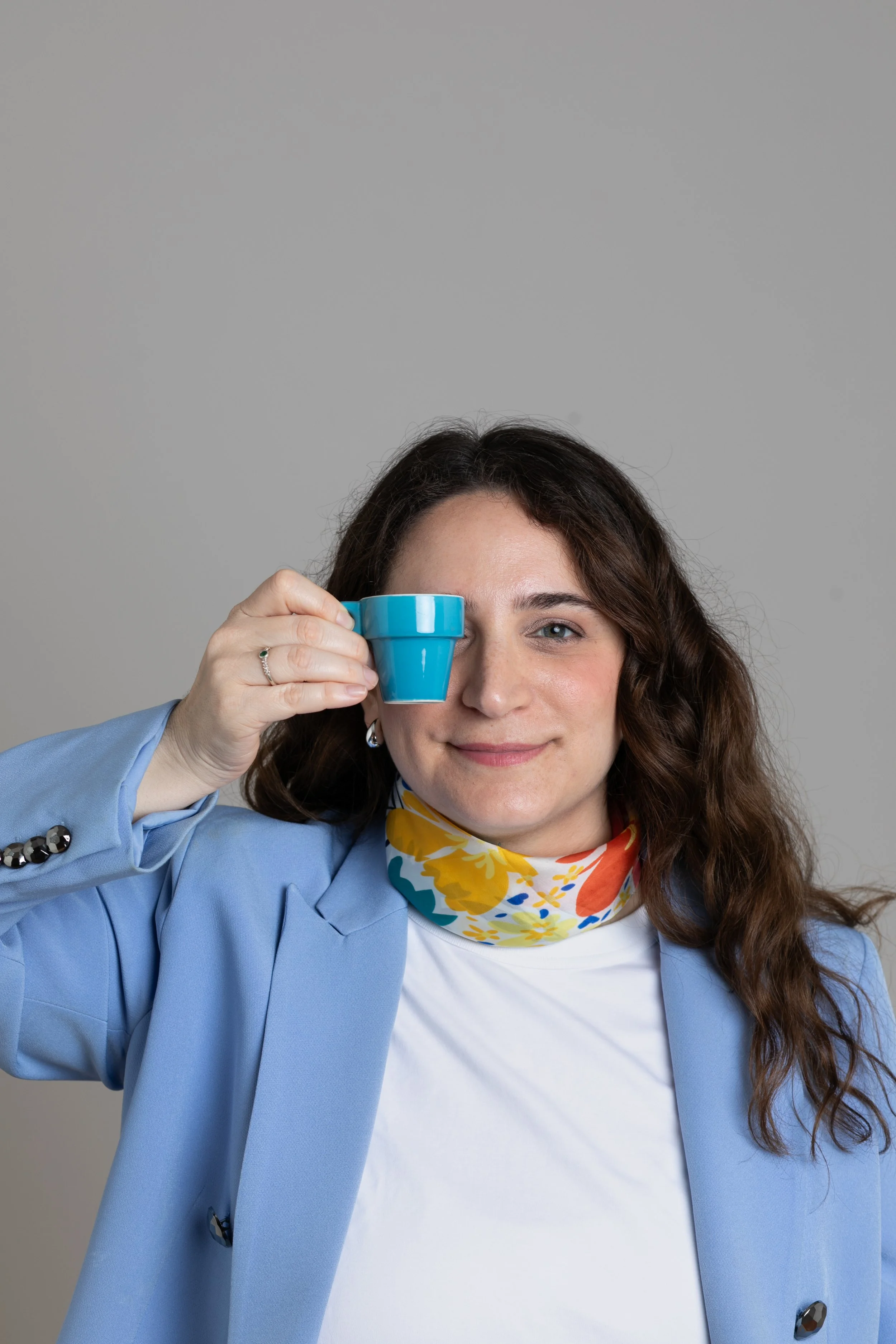 Mujer con cabello rizado y vestido azul, sosteniendo una taza azul frente a un ojo con una expresión sonriente y sin miedo.