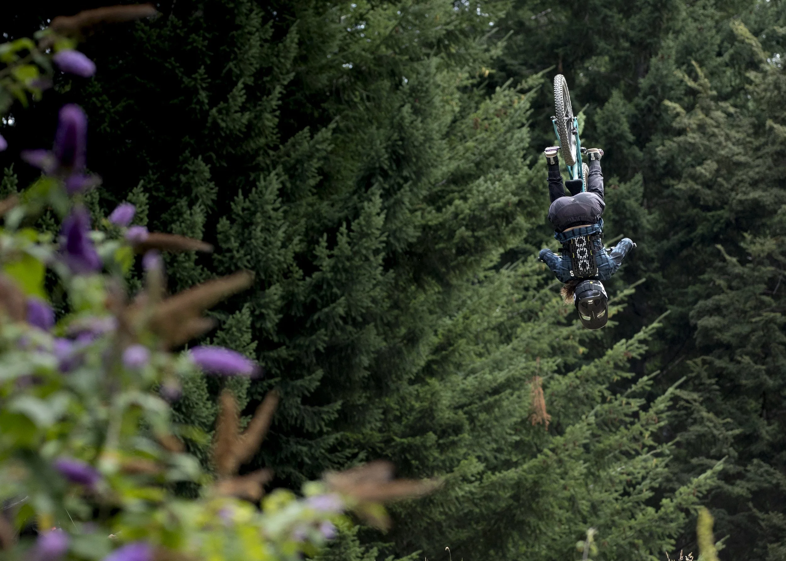 Person performing a backflip on a mountain bike in a forested area.