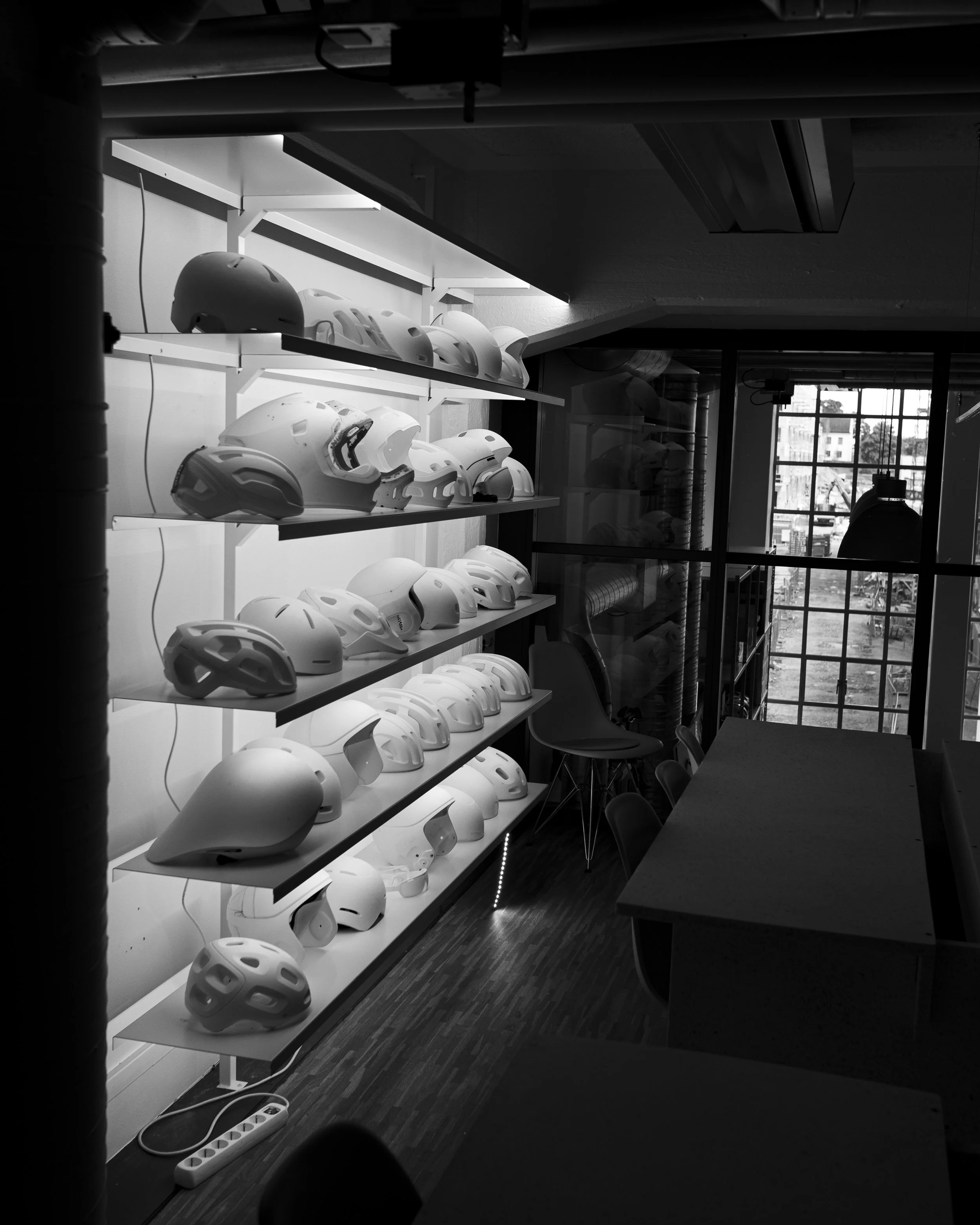 Display of multiple bicycle helmets on white shelves in a modern indoor setting with a large window.
