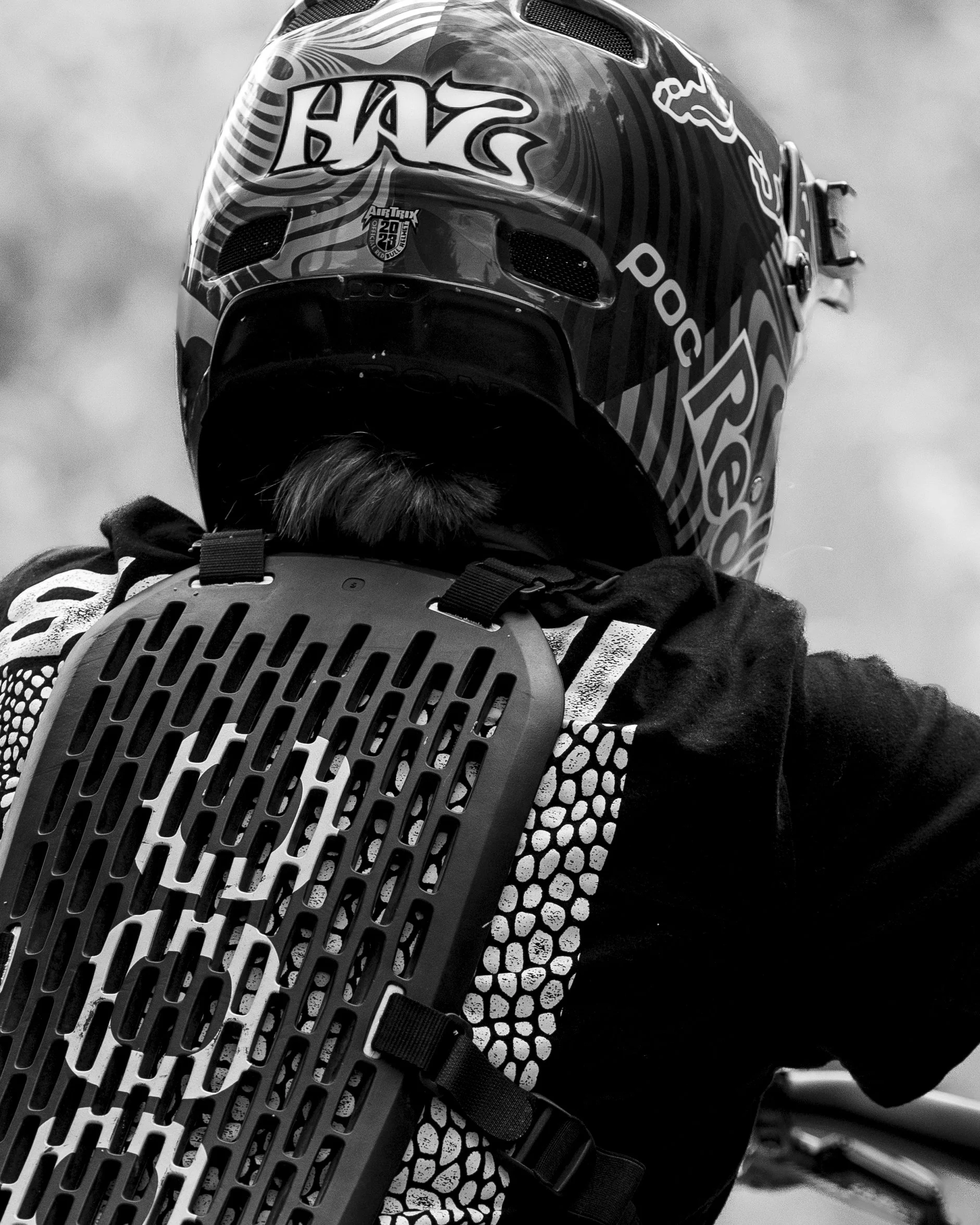 Close-up of a person wearing a motocross helmet and protective gear, with a ventilation device attached to their back.