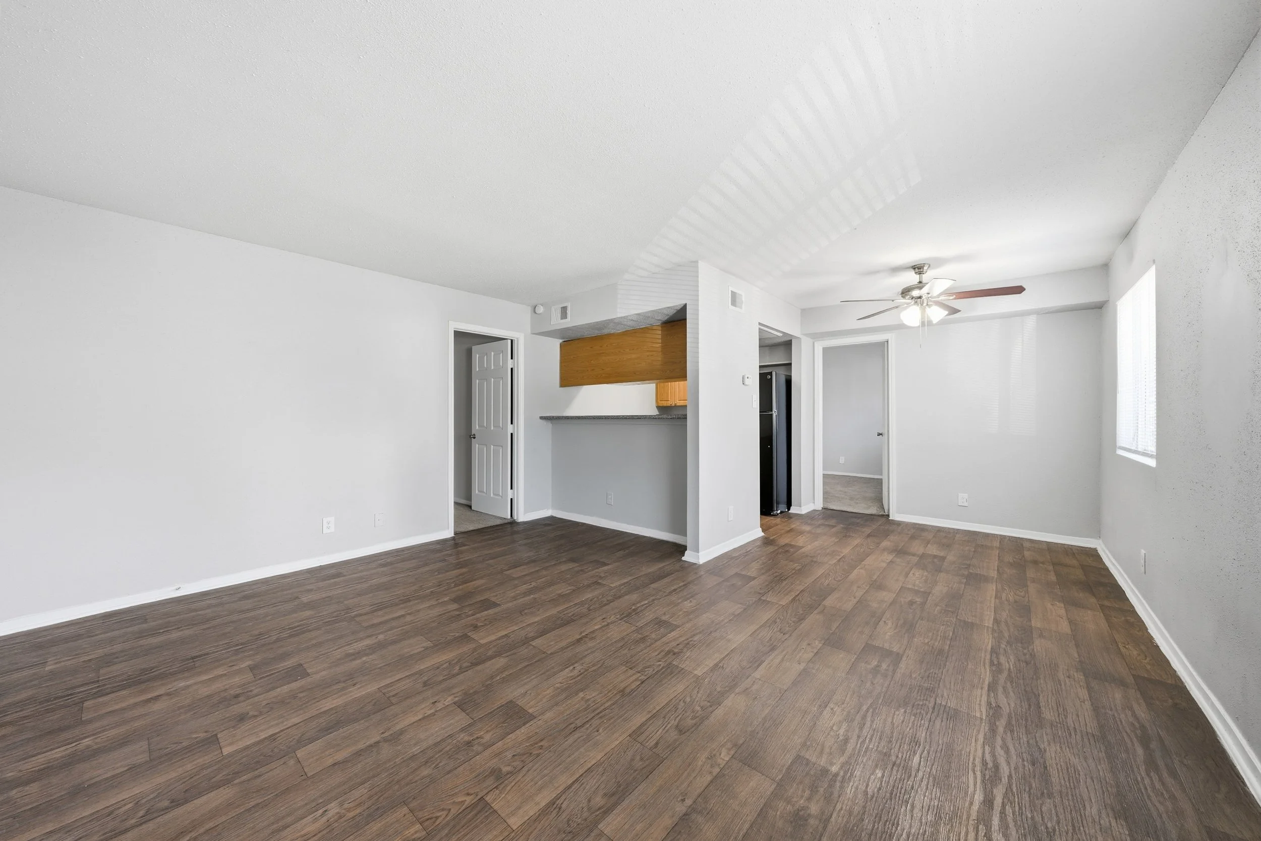 Empty living room with wood flooring, white walls, a ceiling fan, and two windows.