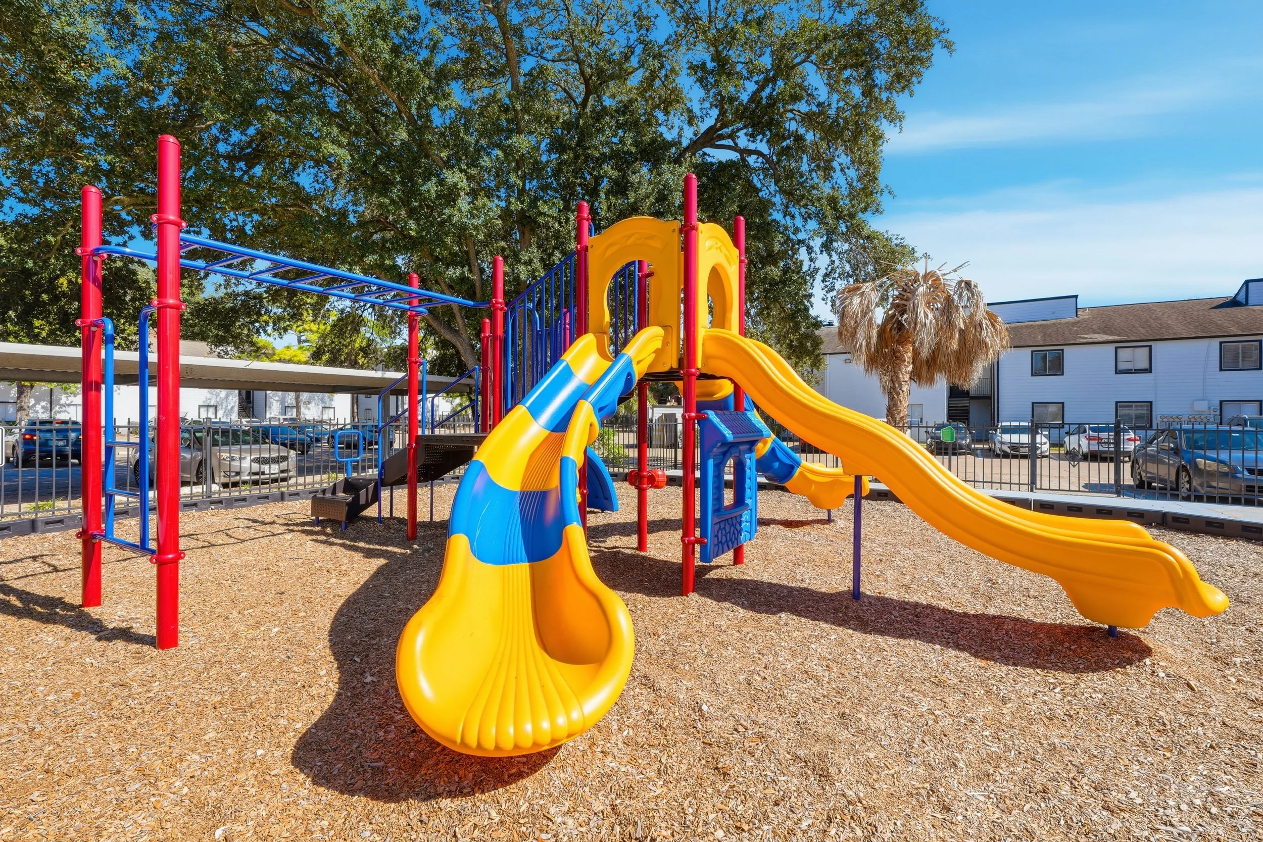 Colorful playground with slides and climbing structures near trees and parked cars.