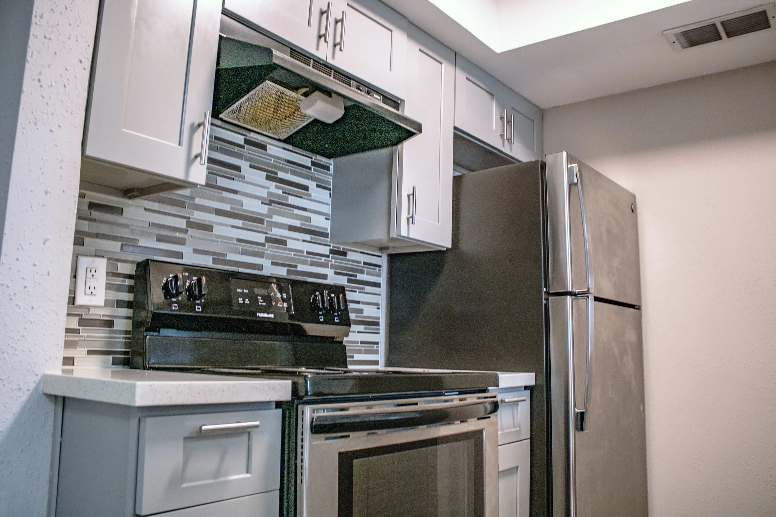 Kitchen with white cabinets, a black stove, stainless steel refrigerator, mosaic tile backsplash, and speckled countertop.