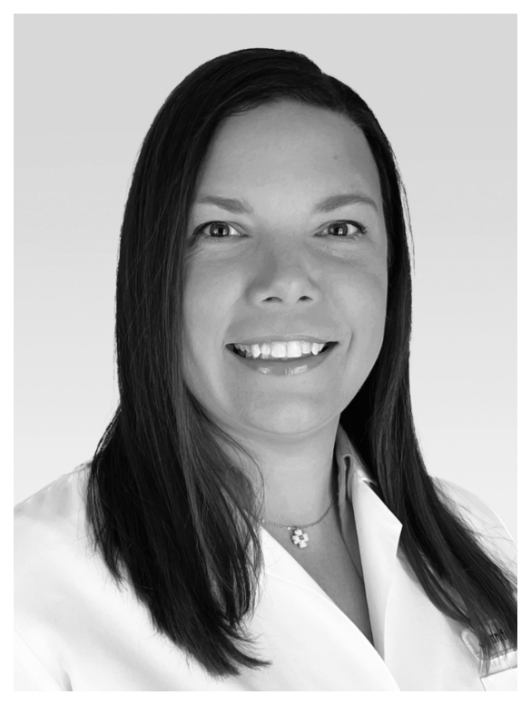 Black and white portrait of a woman with straight dark hair, smiling, wearing a collared shirt and a necklace with a flower pendant.