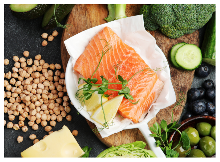 Fresh salmon fillets on a plate with lemon, surrounded by vegetables and chickpeas.