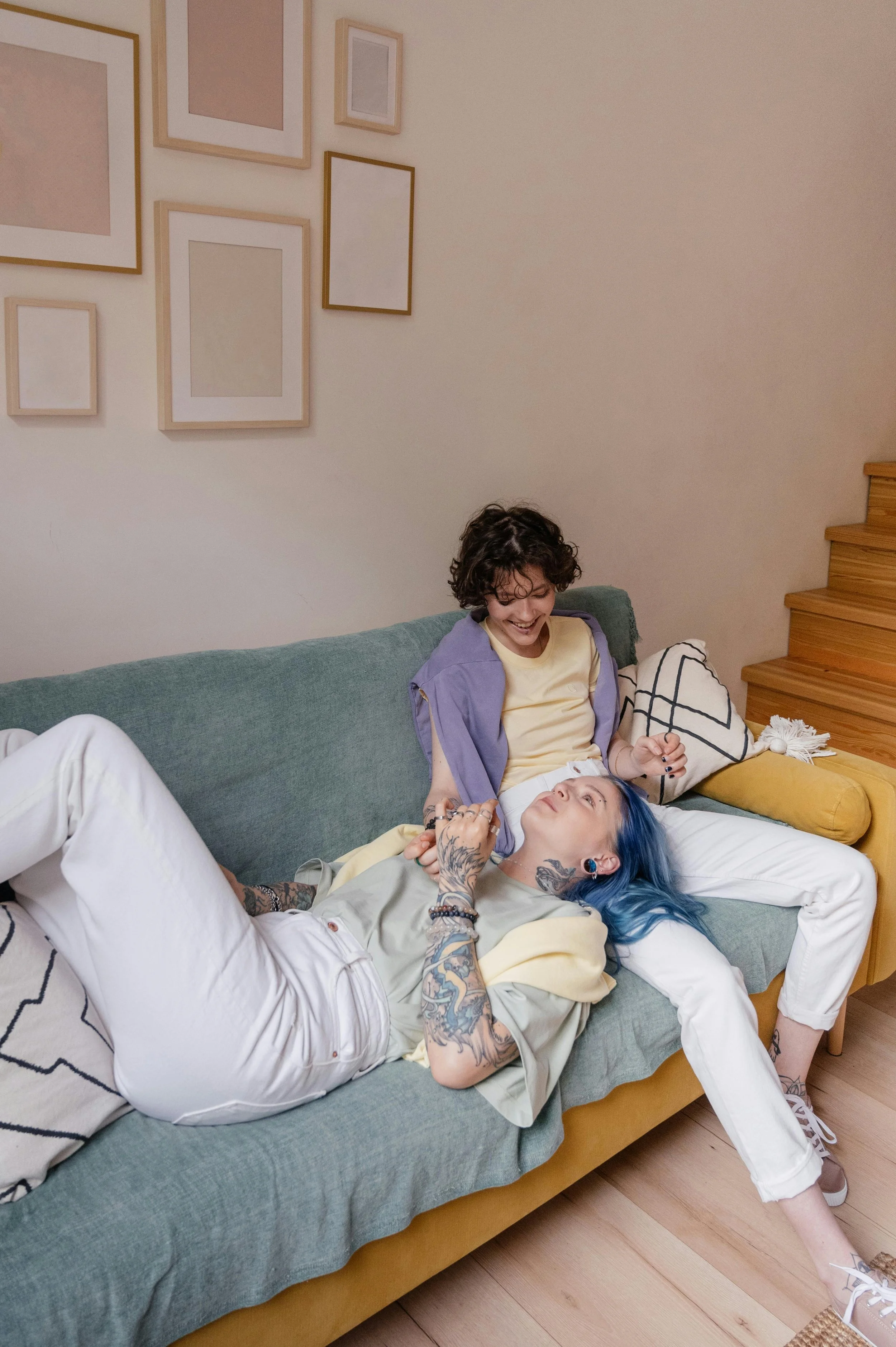 Two people relaxing on a couch, one lying down with their head in the other's lap while they hold hands, in a living room setting.