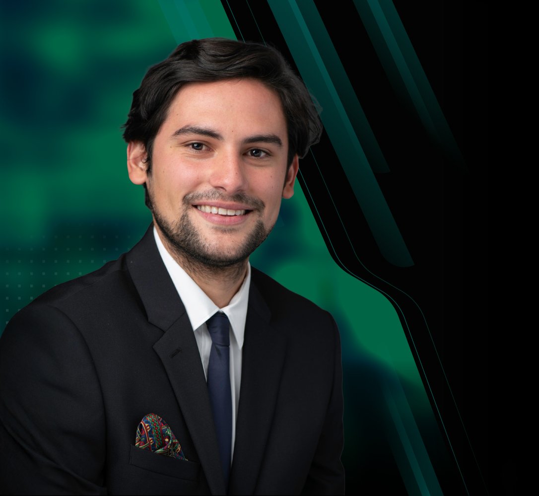 A young man in a suit with a white shirt, dark tie, and colorful pocket square, smiling against a dark green and black abstract background.