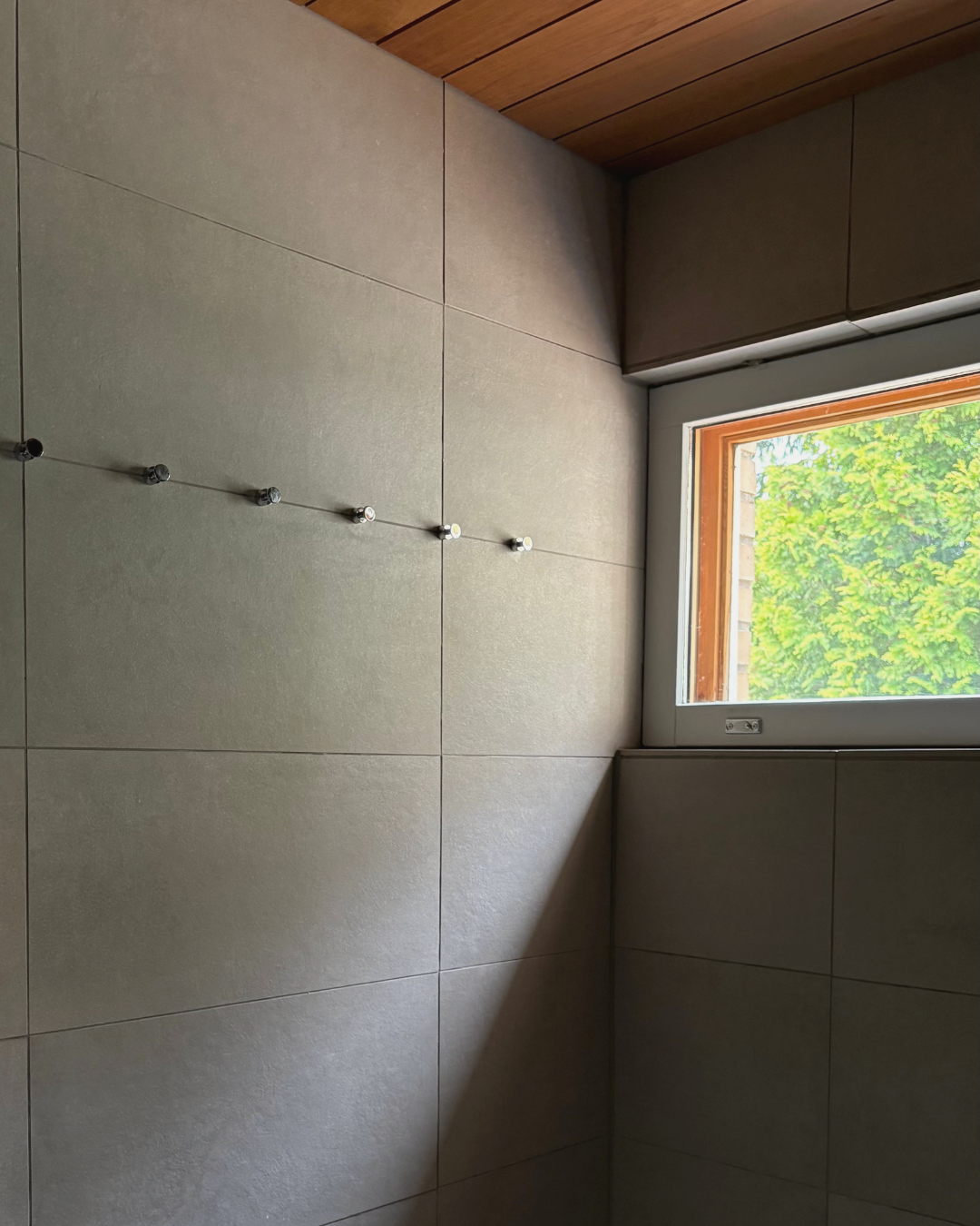 Kuvassa kylpyhuoneen seinä ja minimalistiset laatat, pieniä metallisia koukkuja rivissä seinällä.