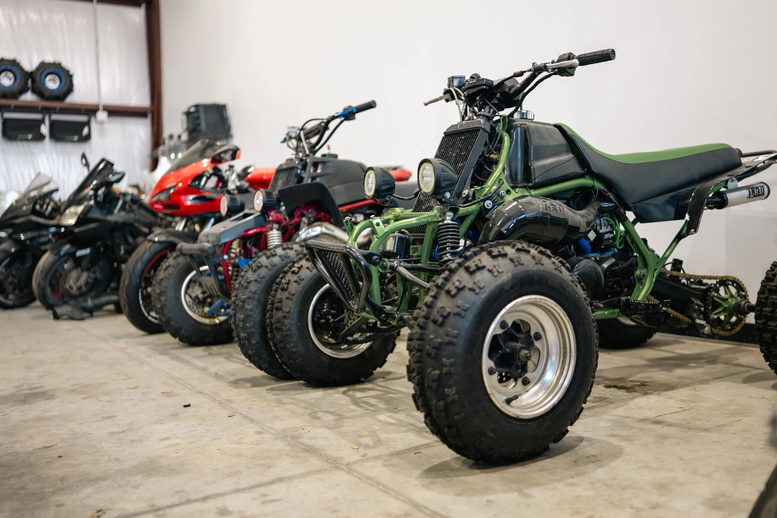 Multiple motorcycles and all-terrain vehicles parked indoors, with the green ATV in the foreground.