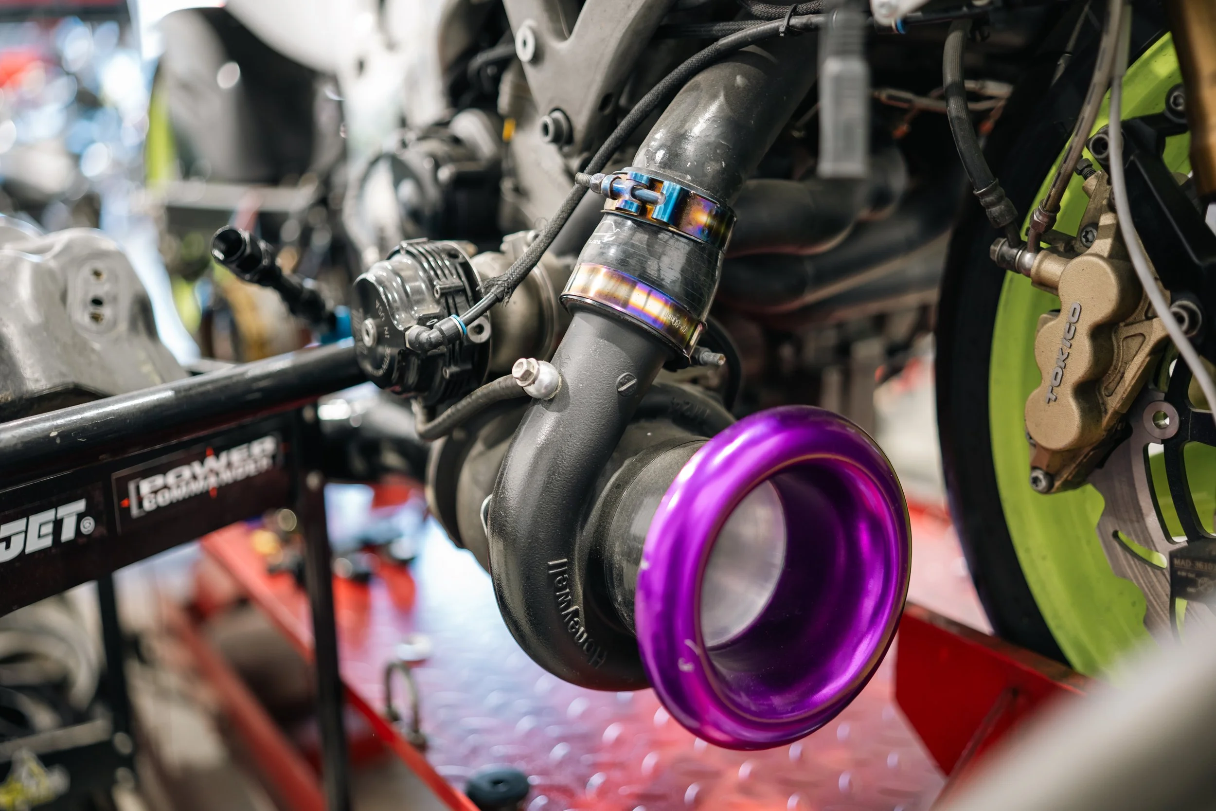 Close-up of a car engine with a purple turbocharger and green brake calipers in the background.