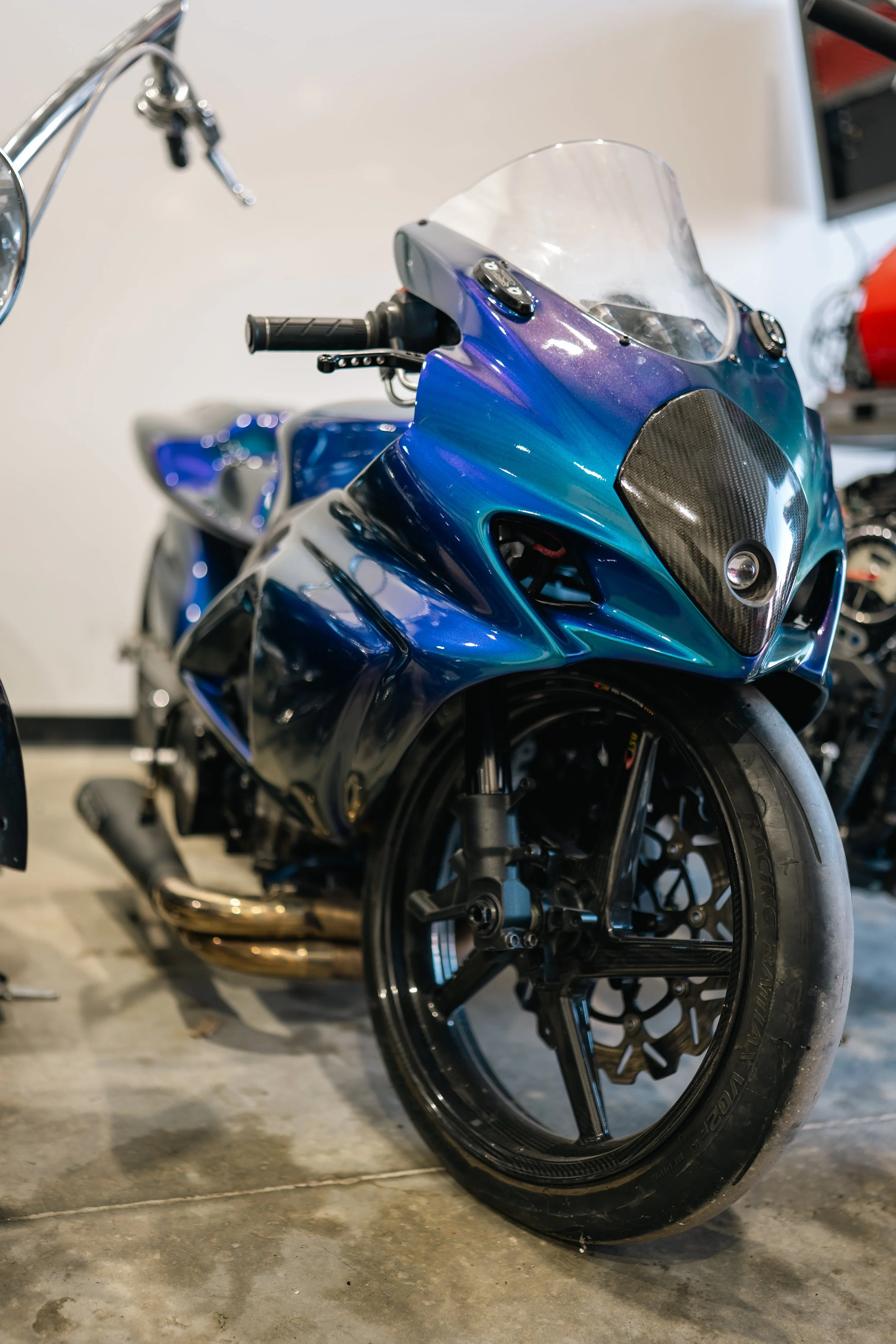 Close-up of a blue motorcycle with a black front tire and tinted windshield parked indoors.