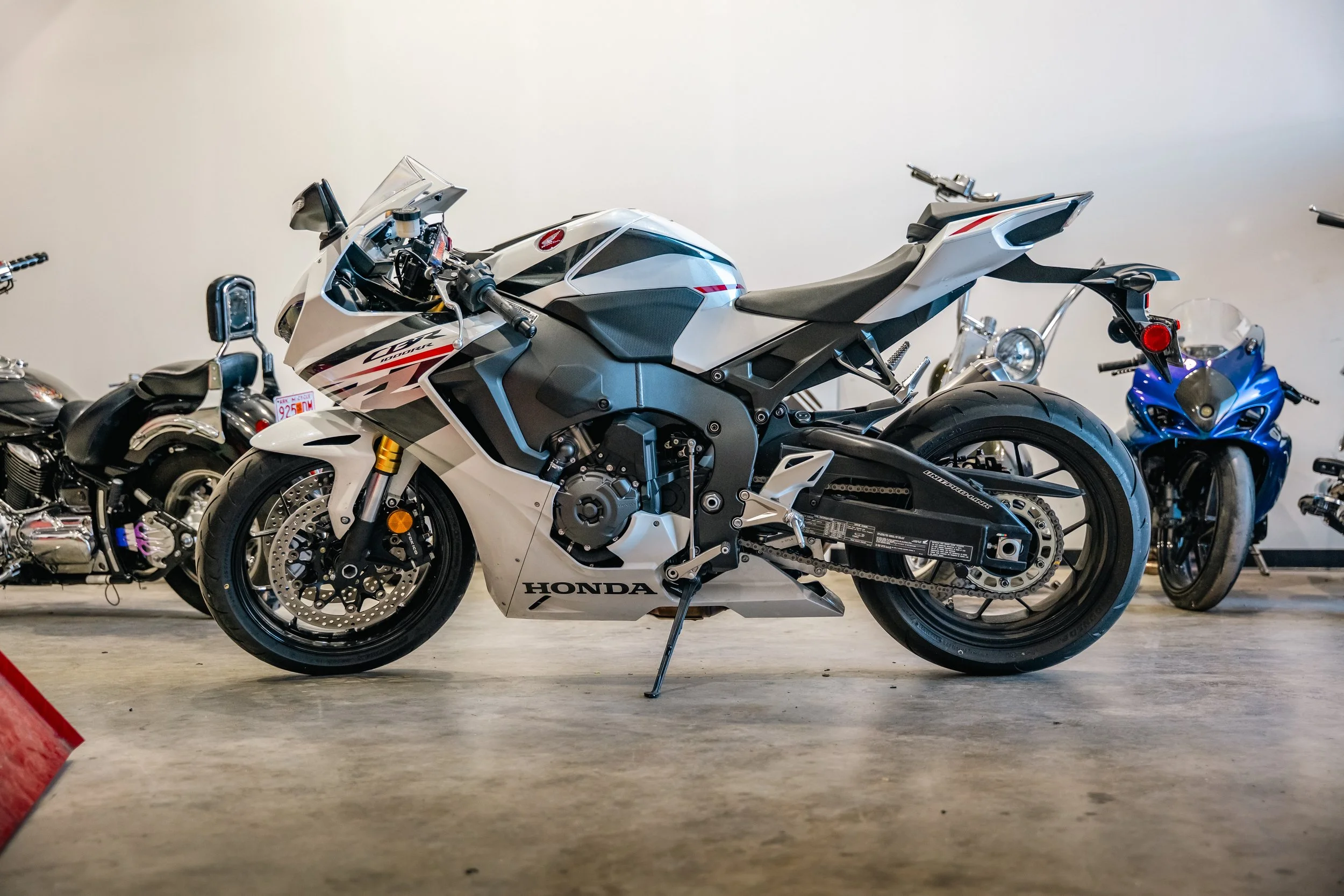 White and black Honda motorcycle parked indoors with other motorcycles in the background.