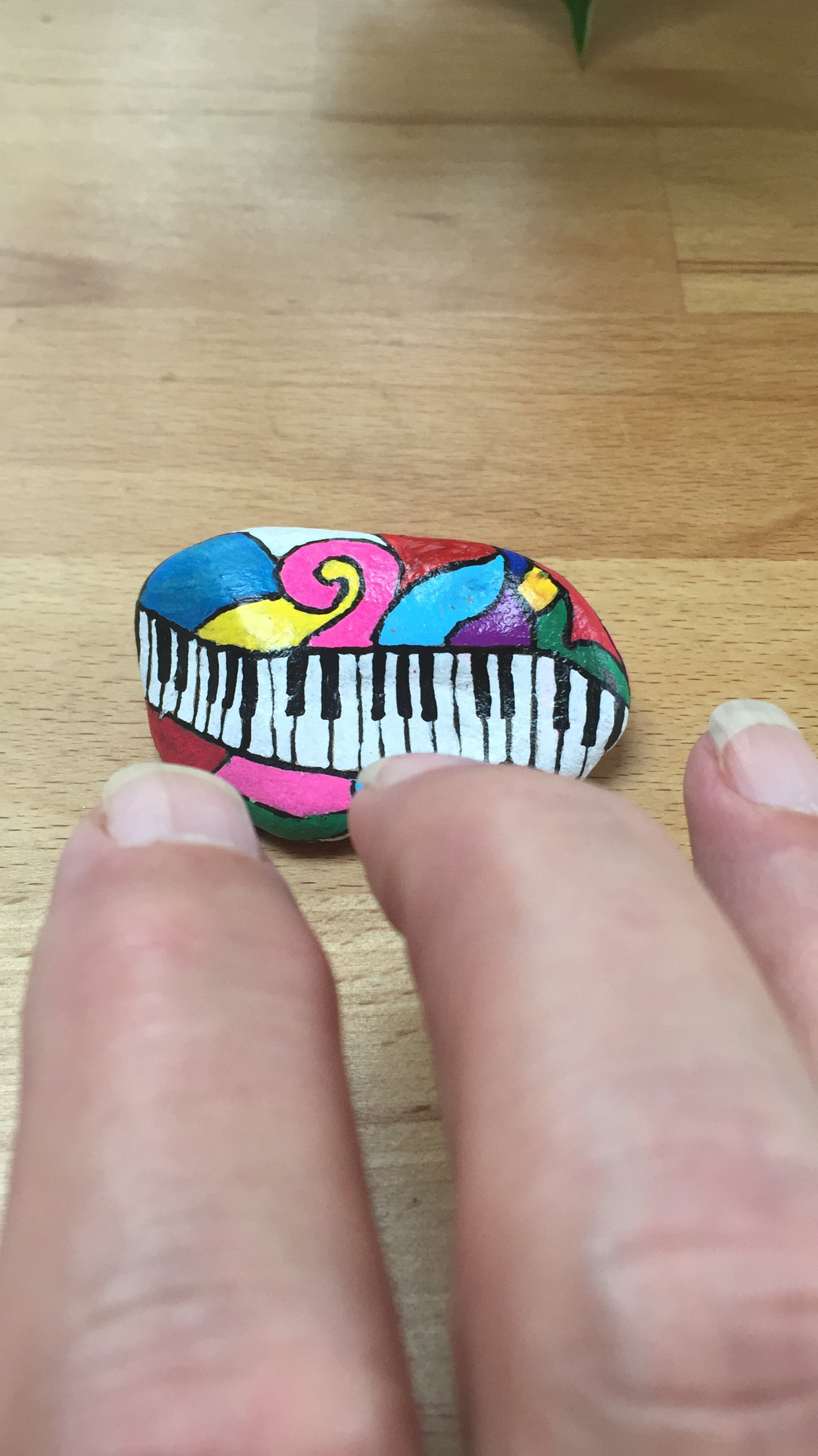 Ein bemalter Stein mit einer bunten, künstlerischen Darstellung eines Klaviers, umgeben von farbigen Formen.