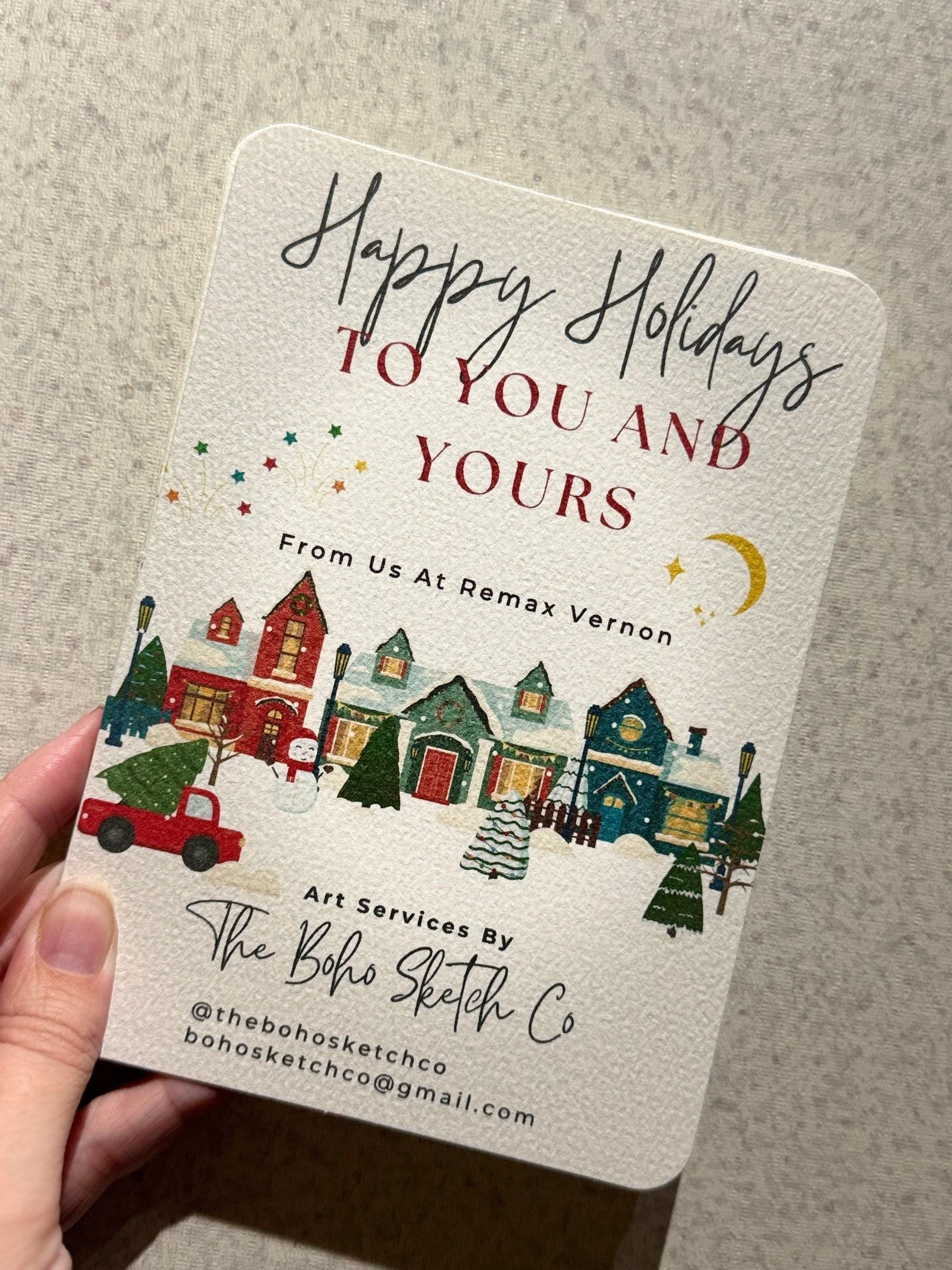 Holiday greeting card with colorful houses, trees, a snowman, and a red truck, wishing happy holidays from Remax Vernon and The Boho Sketch Co.