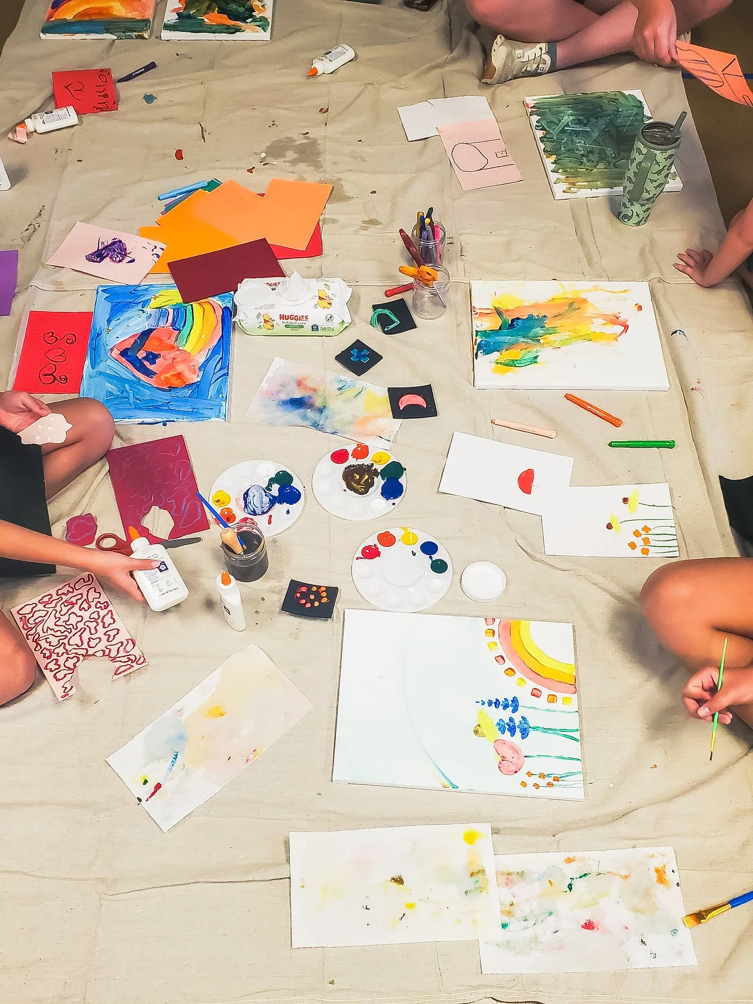 Various colorful abstract paintings and drawing materials on a cloth-covered surface.