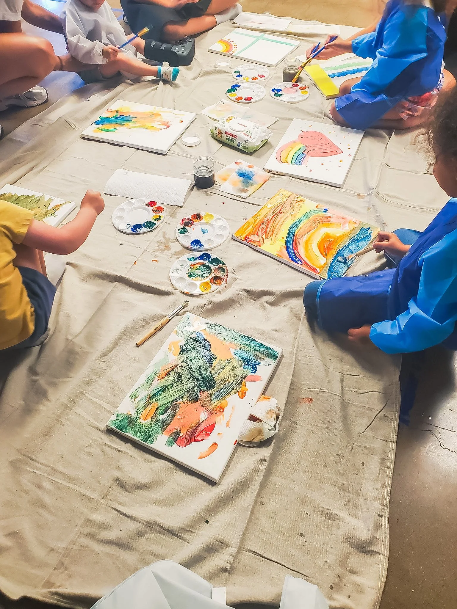 Children painting colorful pictures on canvases during an art activity, with art supplies like paints and brushes.