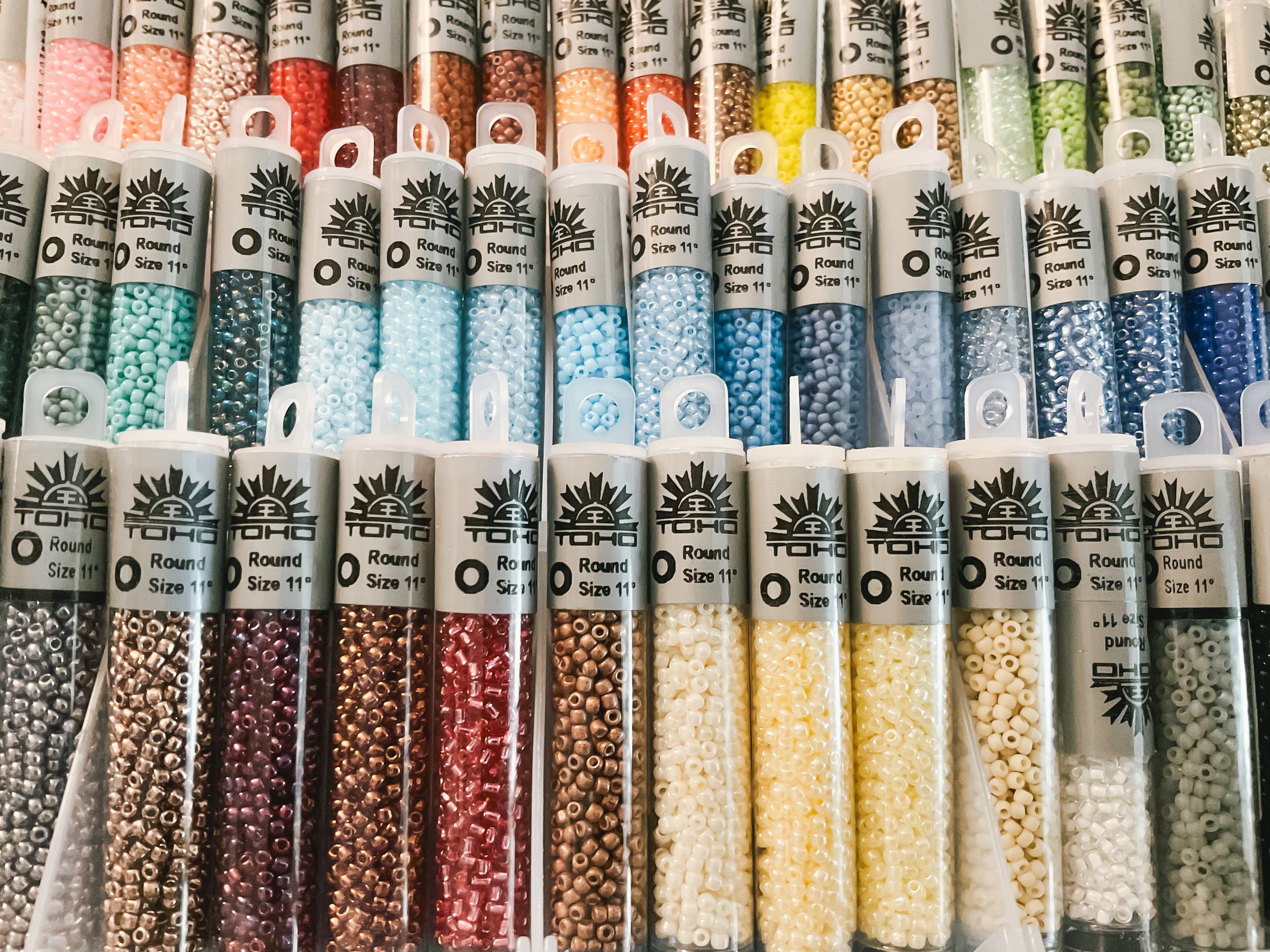 Rows of colorful small beads in clear tubes, arranged by color, with labels indicating they are 11-size round beads from TOHO.