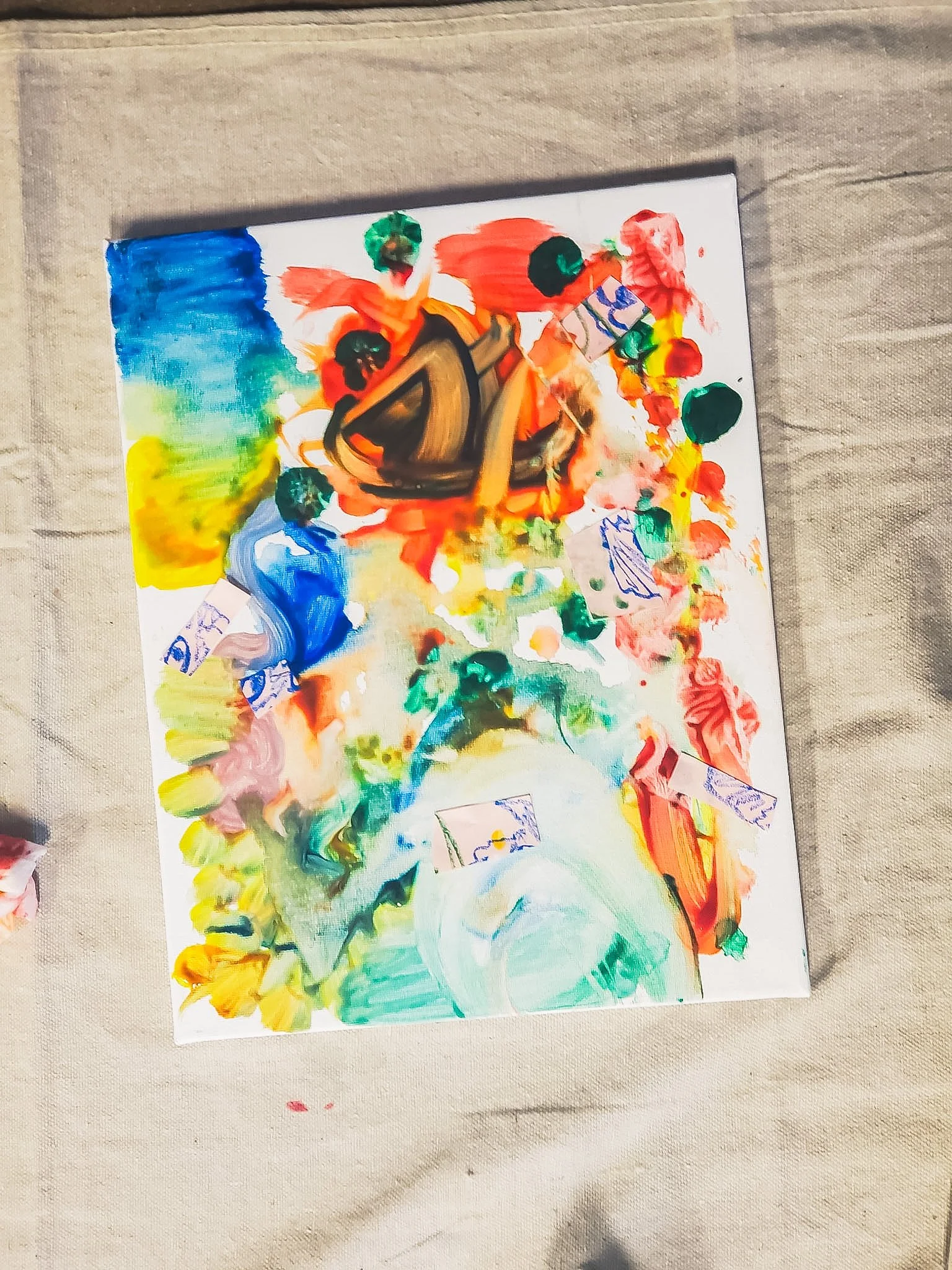 Colorful abstract painting on paper, with splashes of blue, yellow, green, red, and orange paints, and some small sketches or doodles.