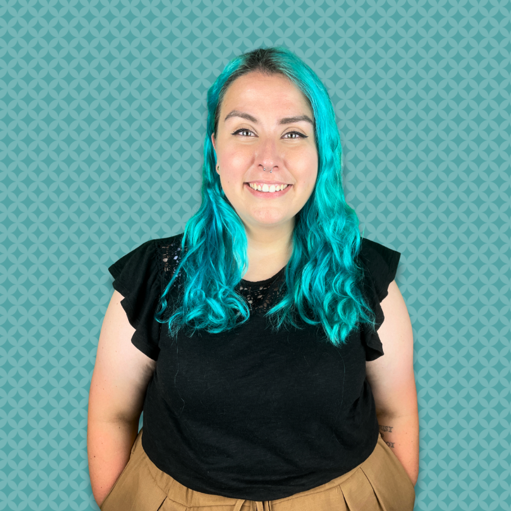 A woman with blue curly hair smiling in front of a light blue patterned background.
