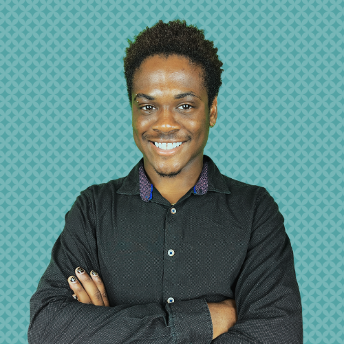 A smiling person with short, wavy hair, wearing dark glasses and a dark polo shirt, standing in front of a teal background with a geometric pattern.
